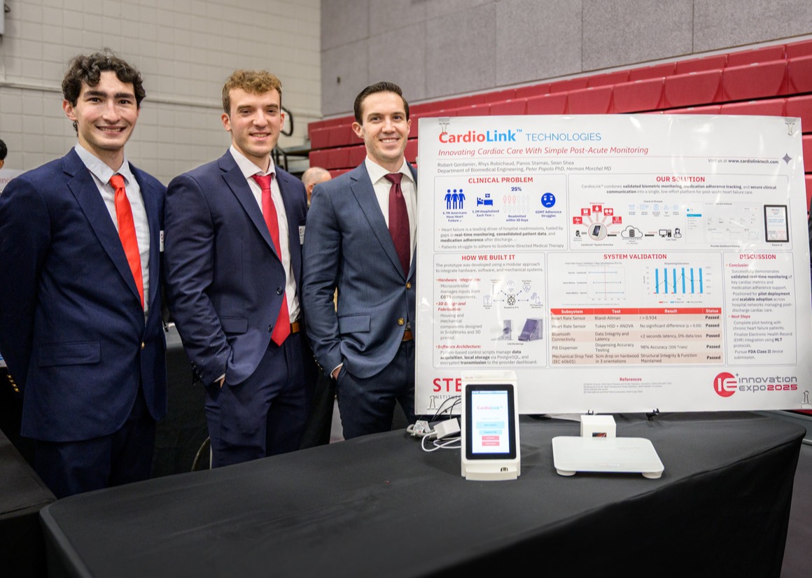 Biomedical engineering alumni Rhys Robichaud, Panos Stamas and Robert Gordanier stand along a posterboard highlighting their project CardioLink.