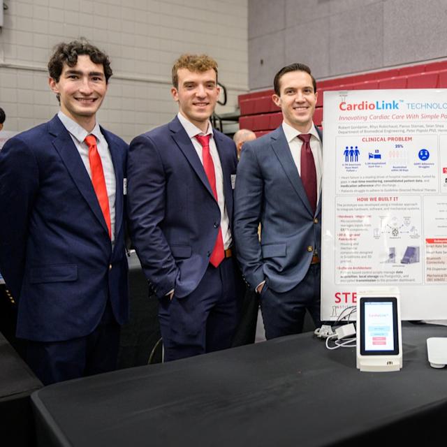 Biomedical engineering alumni Rhys Robichaud, Panos Stamas and Robert Gordanier stand along a posterboard highlighting their project CardioLink.