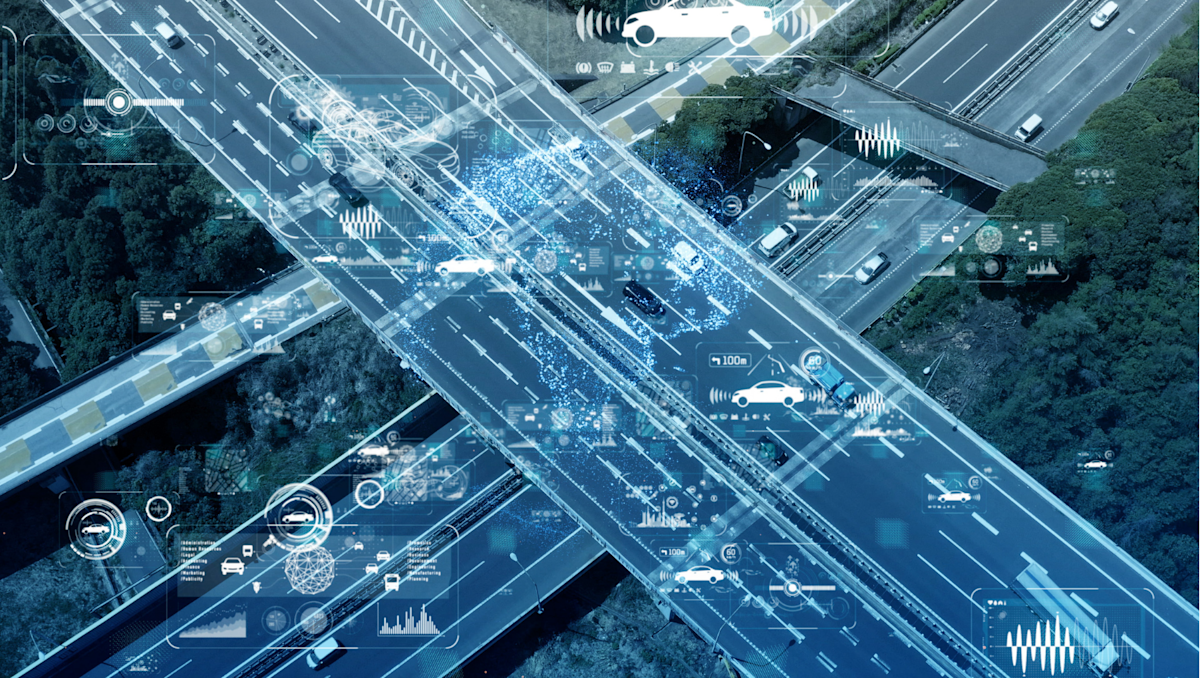Aerial view of a highway interchange overlaid with digital graphics representing connected and autonomous vehicle technology and data.