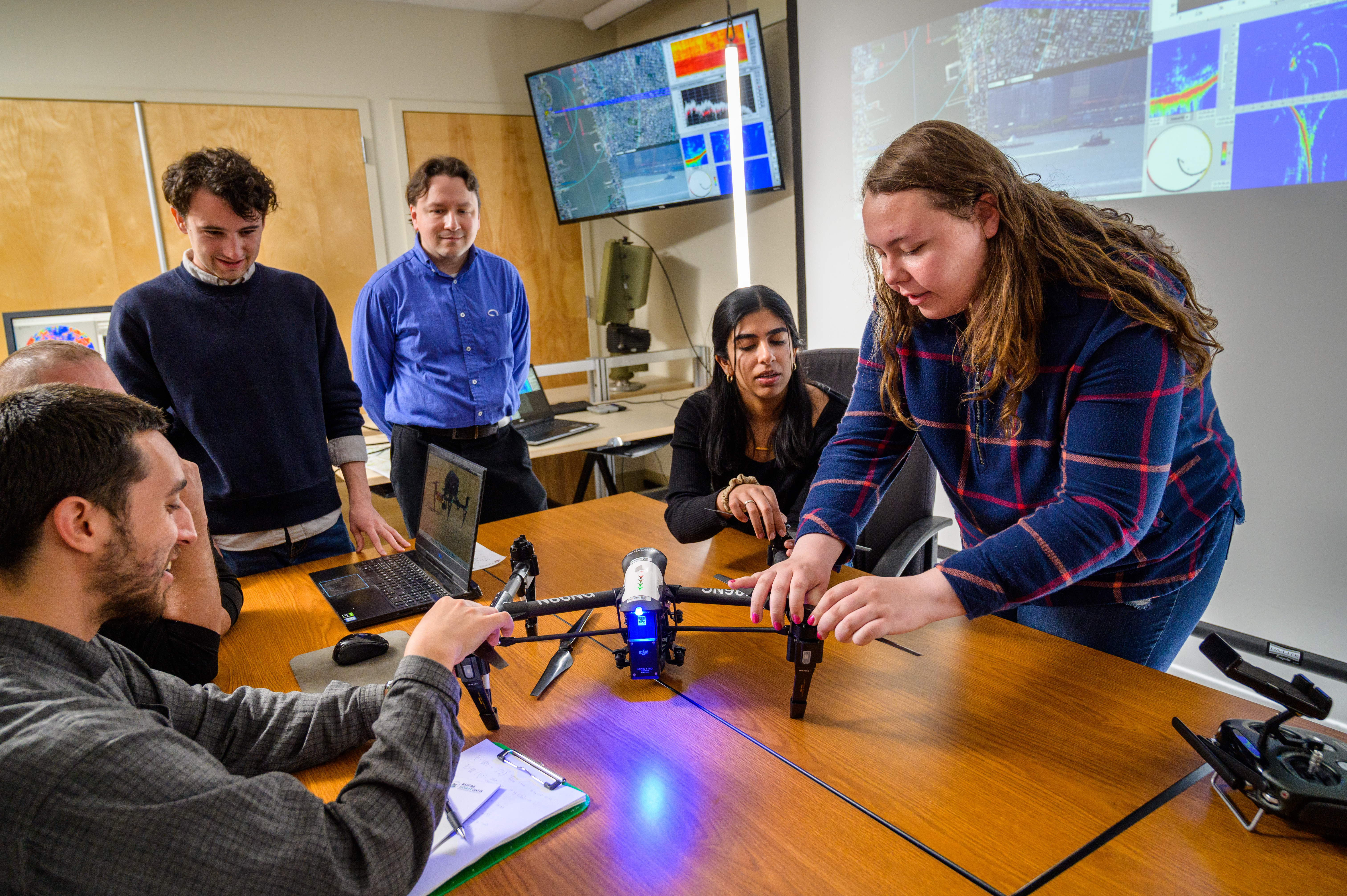 Students and professor adjust a drone in a classroom.