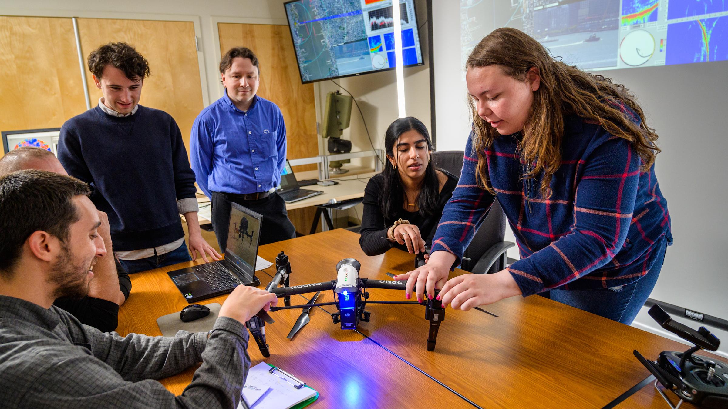 Students and professor adjust a drone in a classroom.