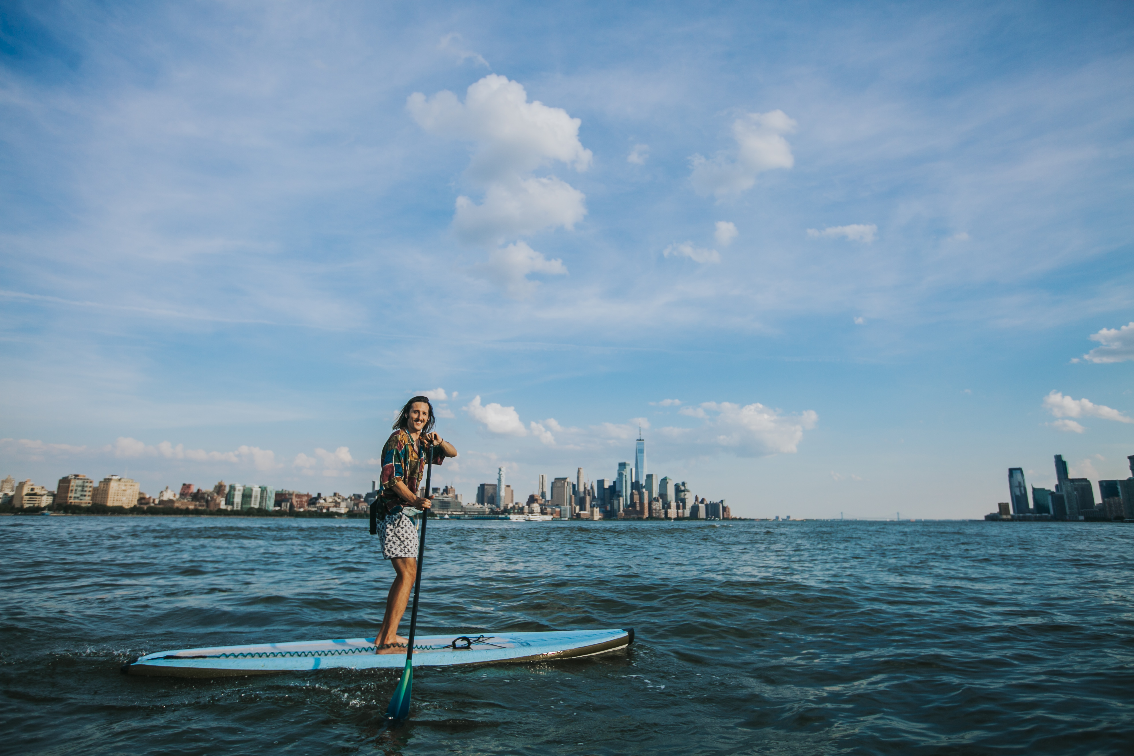 Jeremy Roche stand up paddle boarding on the Hudson River in front of the New York City skyline