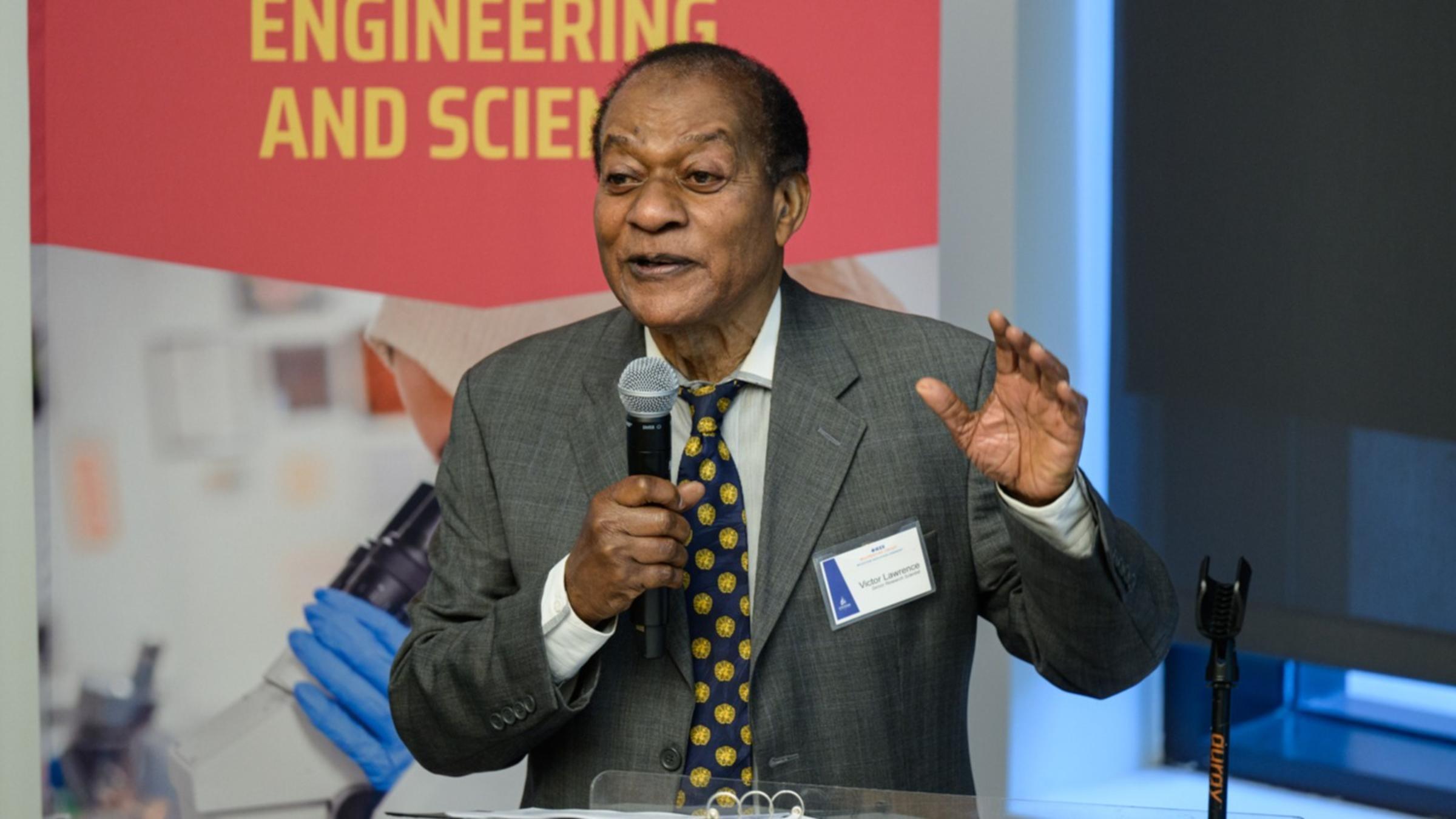Victor Lawrence speaking at a podium with a banner on the left that reads "Schaefer, Jr. School of Engineering and Science".