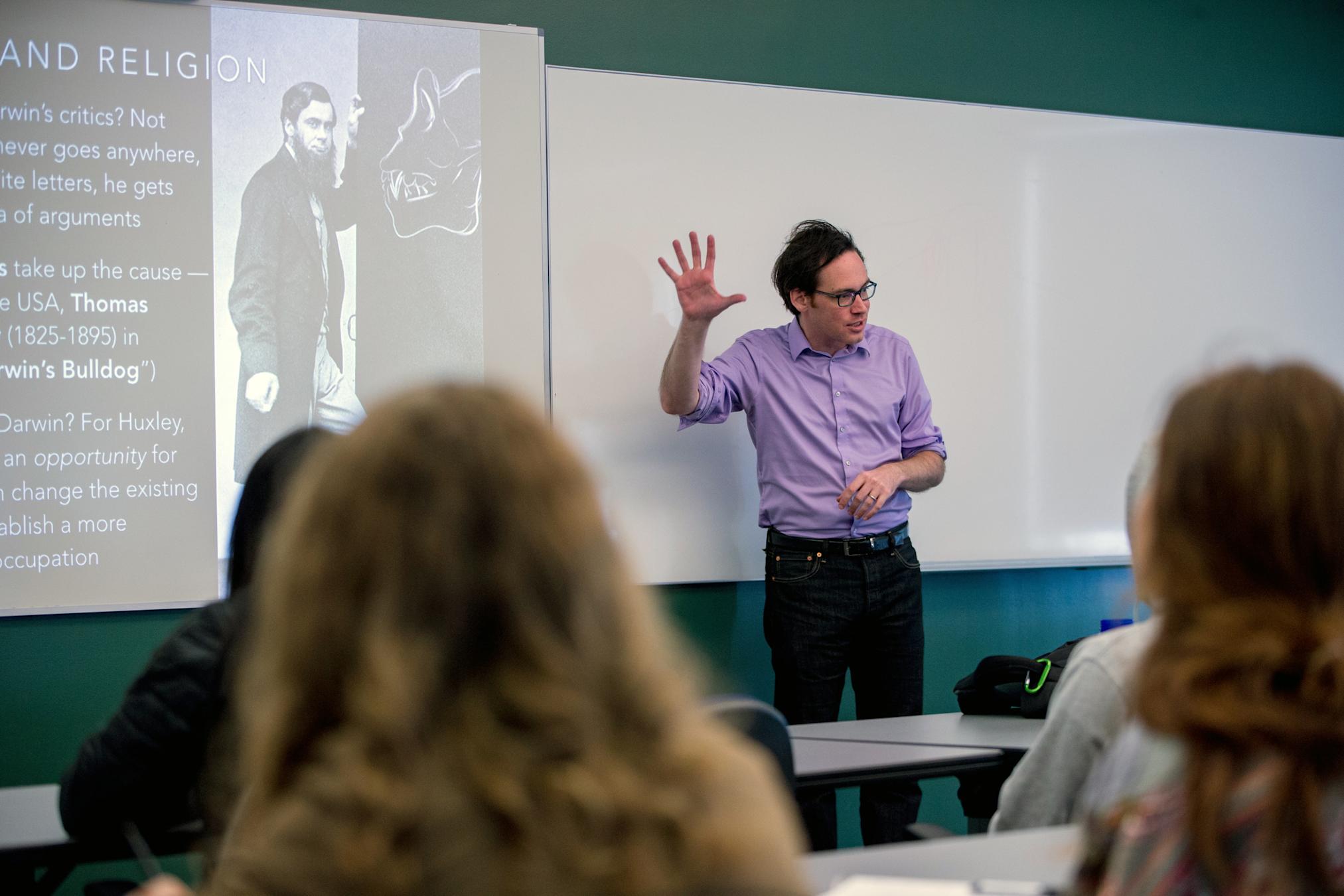 Professor gestures to class in front of presentation