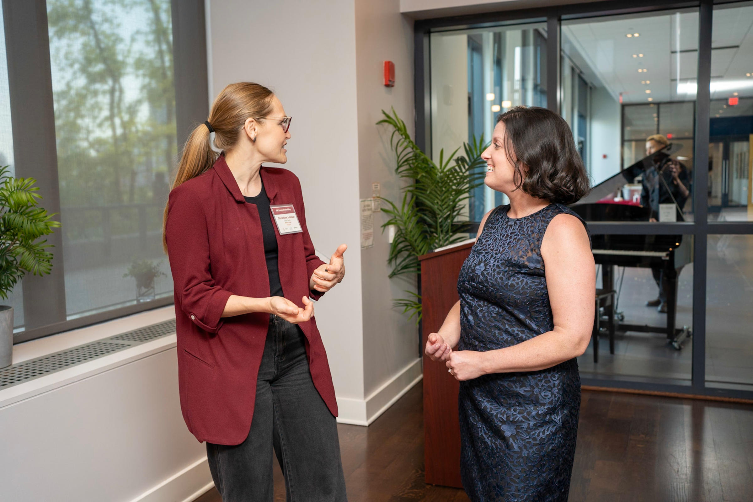 Two women standing with each other smiling and gesturing, having a conversation together.