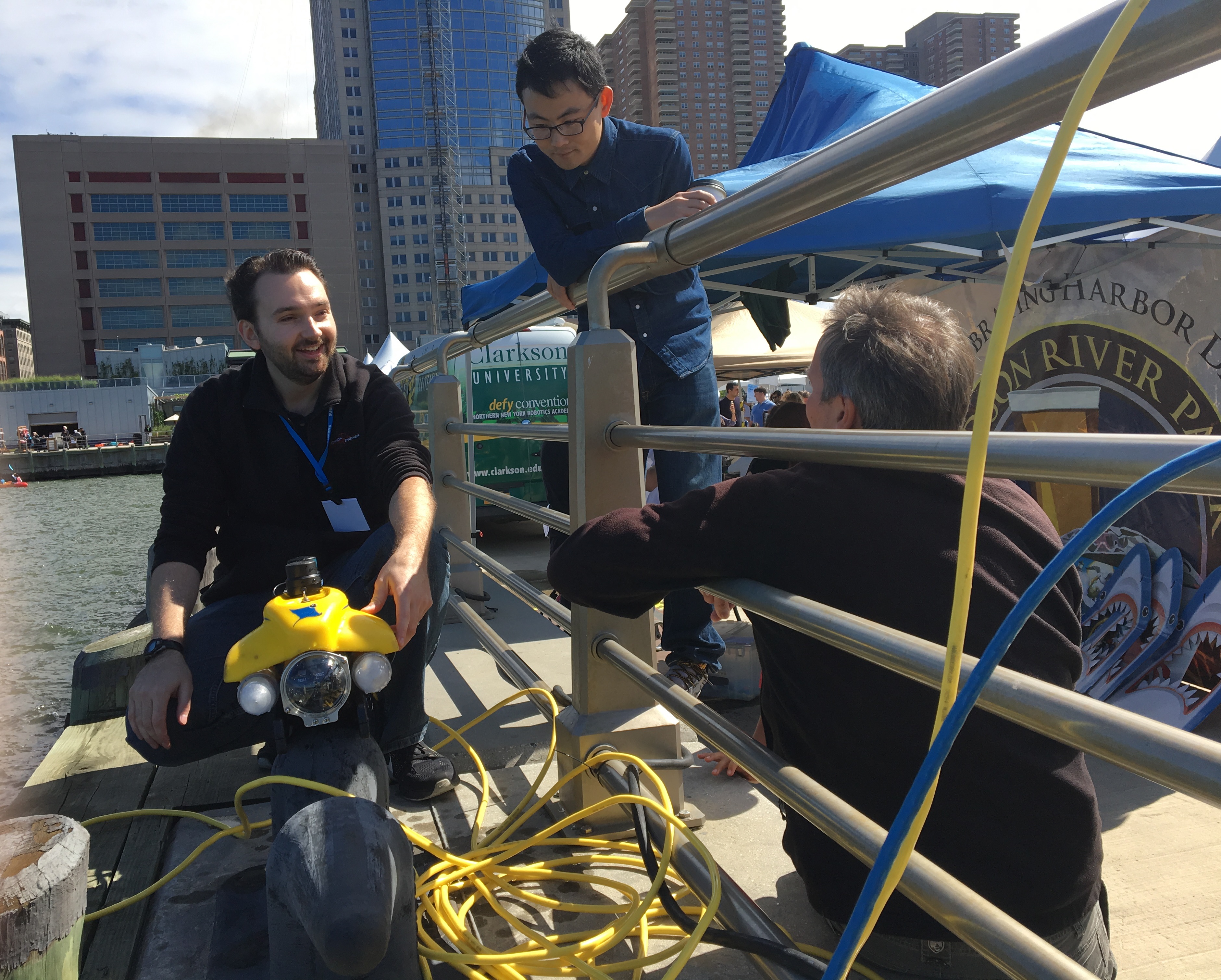 Stevens professor Brendan Englot and two onlookers on a pier with Englat's autonomous water robot.