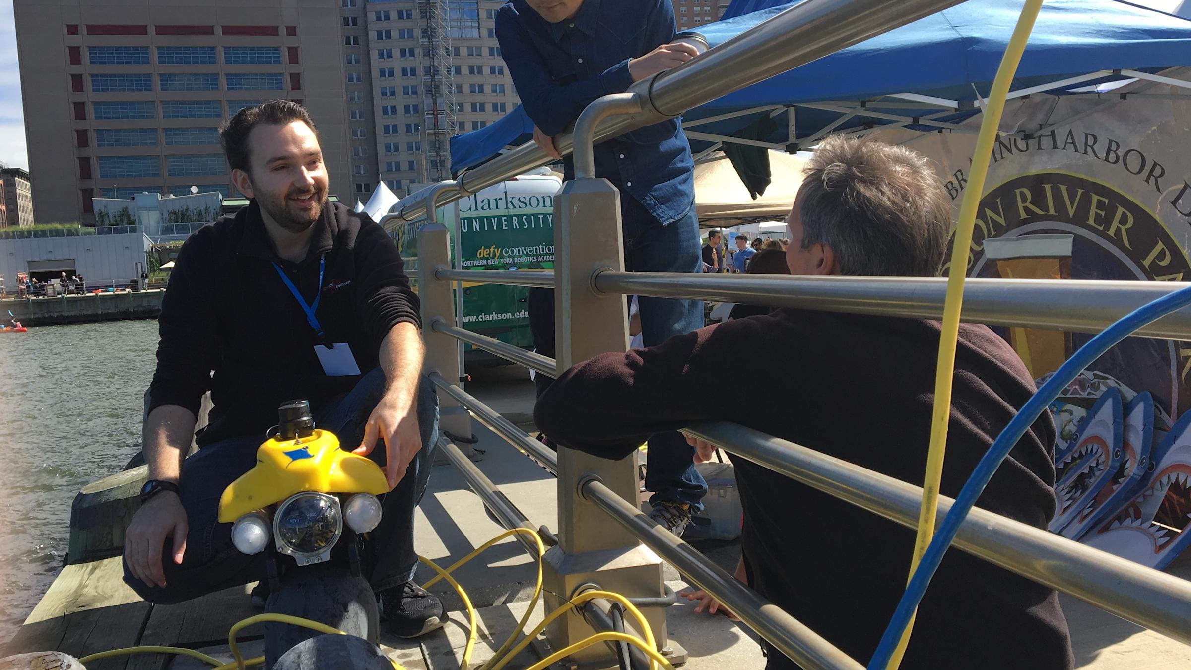 Stevens professor Brendan Englot and two onlookers on a pier with Englat's autonomous water robot.