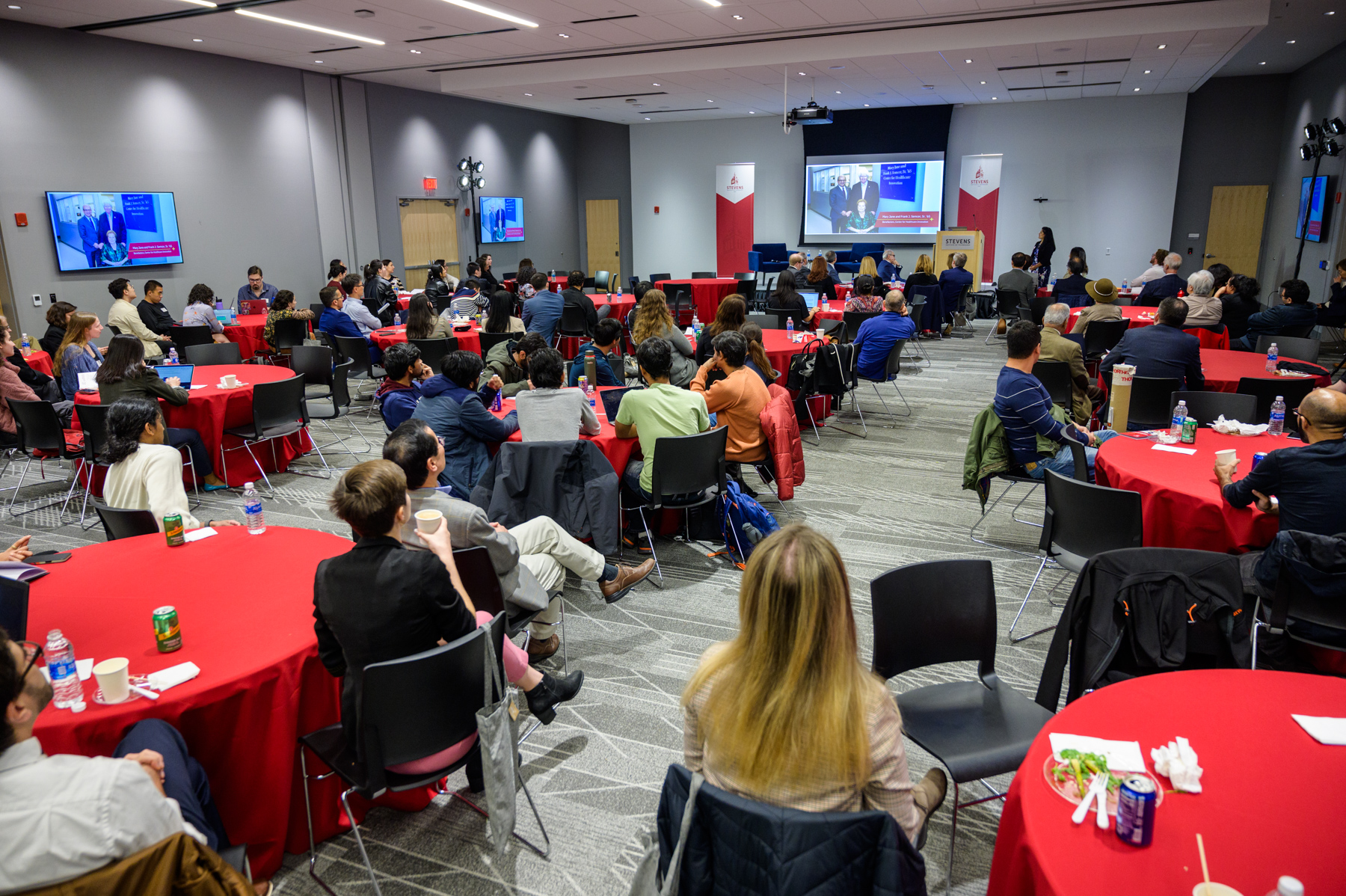 Audience seated at tables, attending the CHI Relaunch event, with several individuals talking to each other.