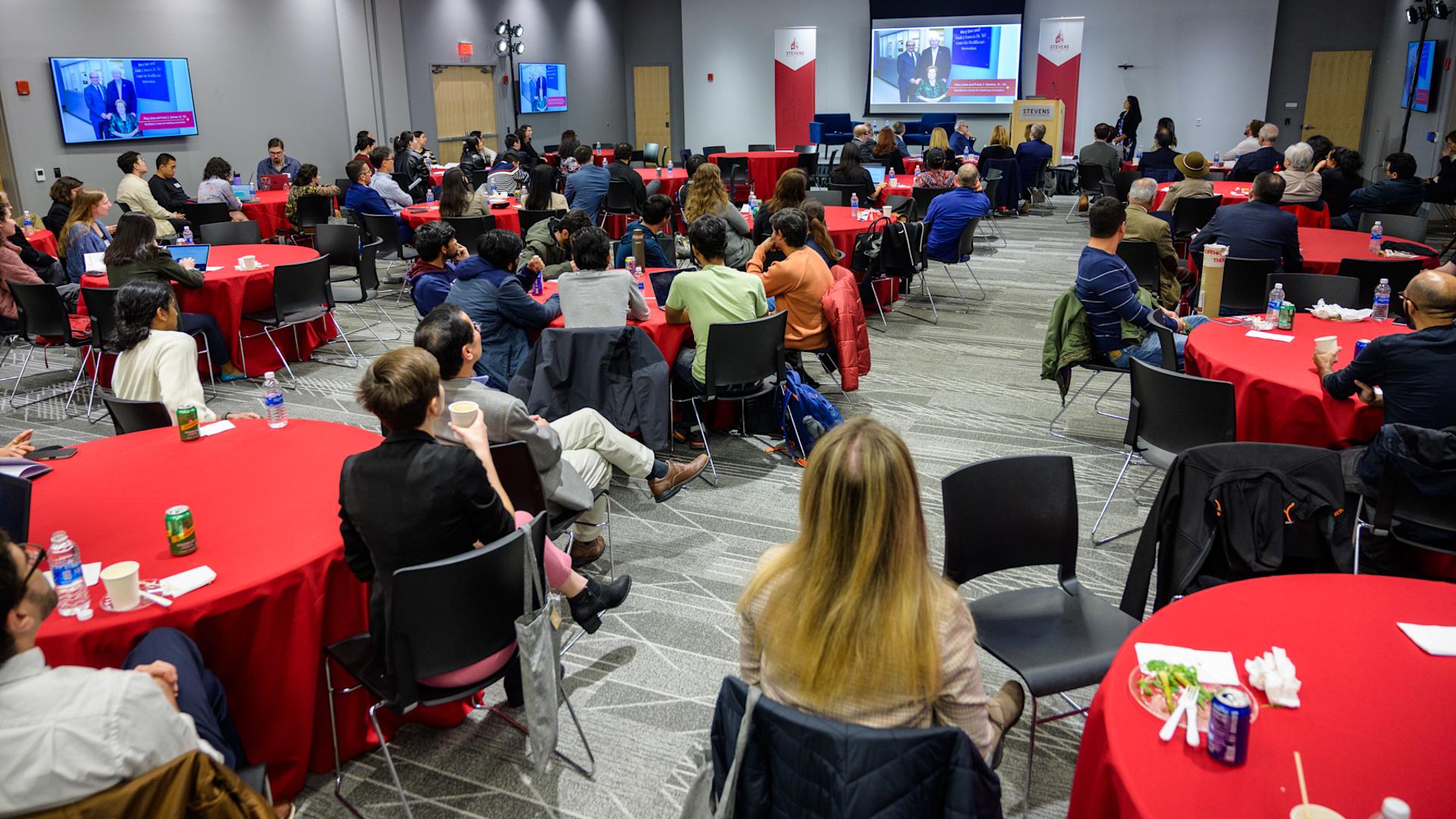 Audience seated at tables, attending the CHI Relaunch event, with several individuals talking to each other.