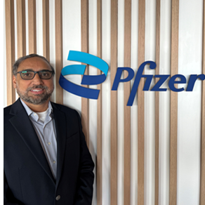 Rupinder Bhullar stands in front of the Pfizer logo.