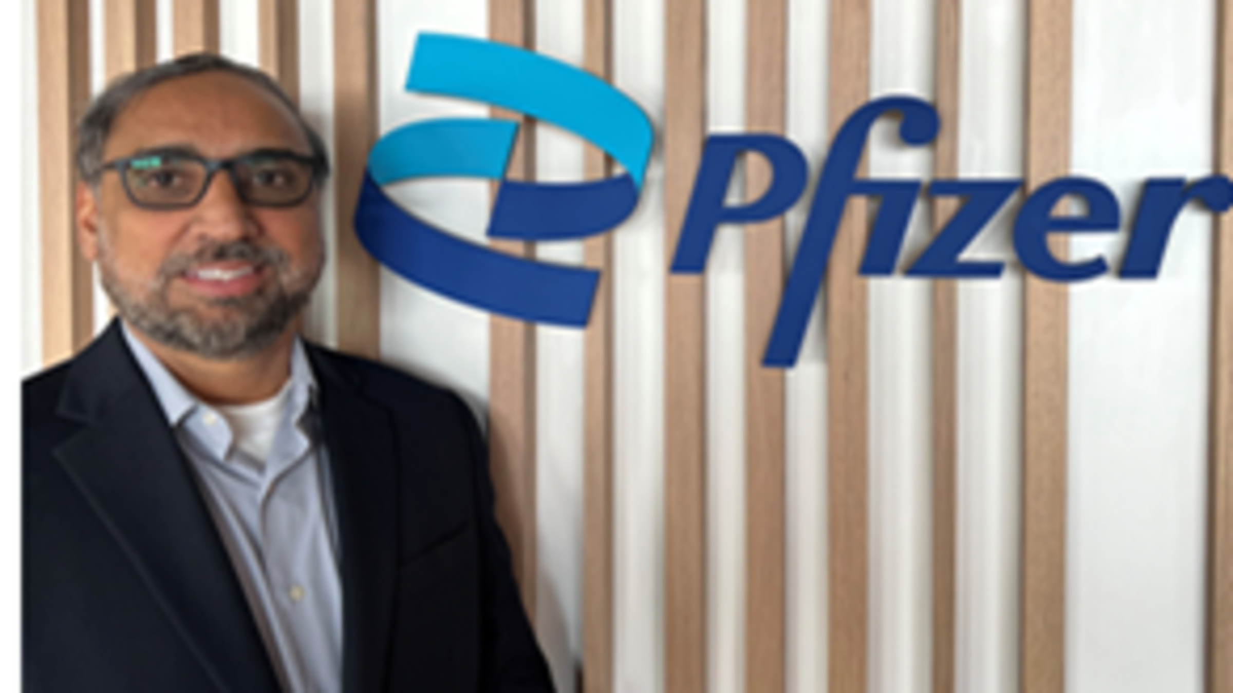 Rupinder Bhullar stands in front of the Pfizer logo.