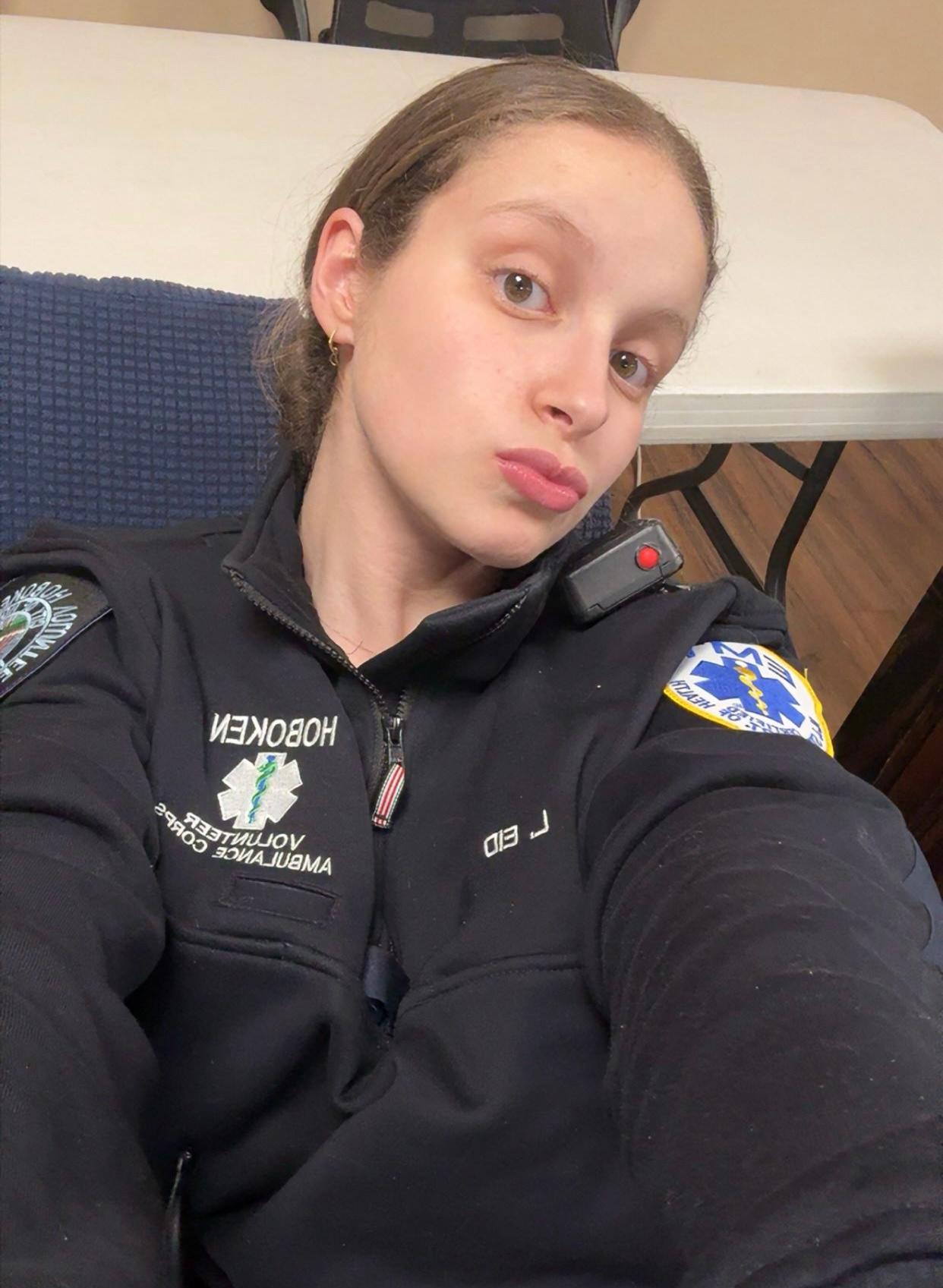 Lilya Eid taking a selfie wearing an emergency medical technician sweatshirt and a radio monitor on her left shoulder. 