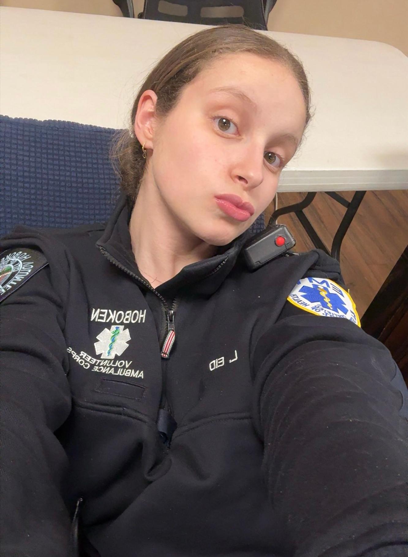 Lilya Eid taking a selfie wearing an emergency medical technician sweatshirt and a radio monitor on her left shoulder.