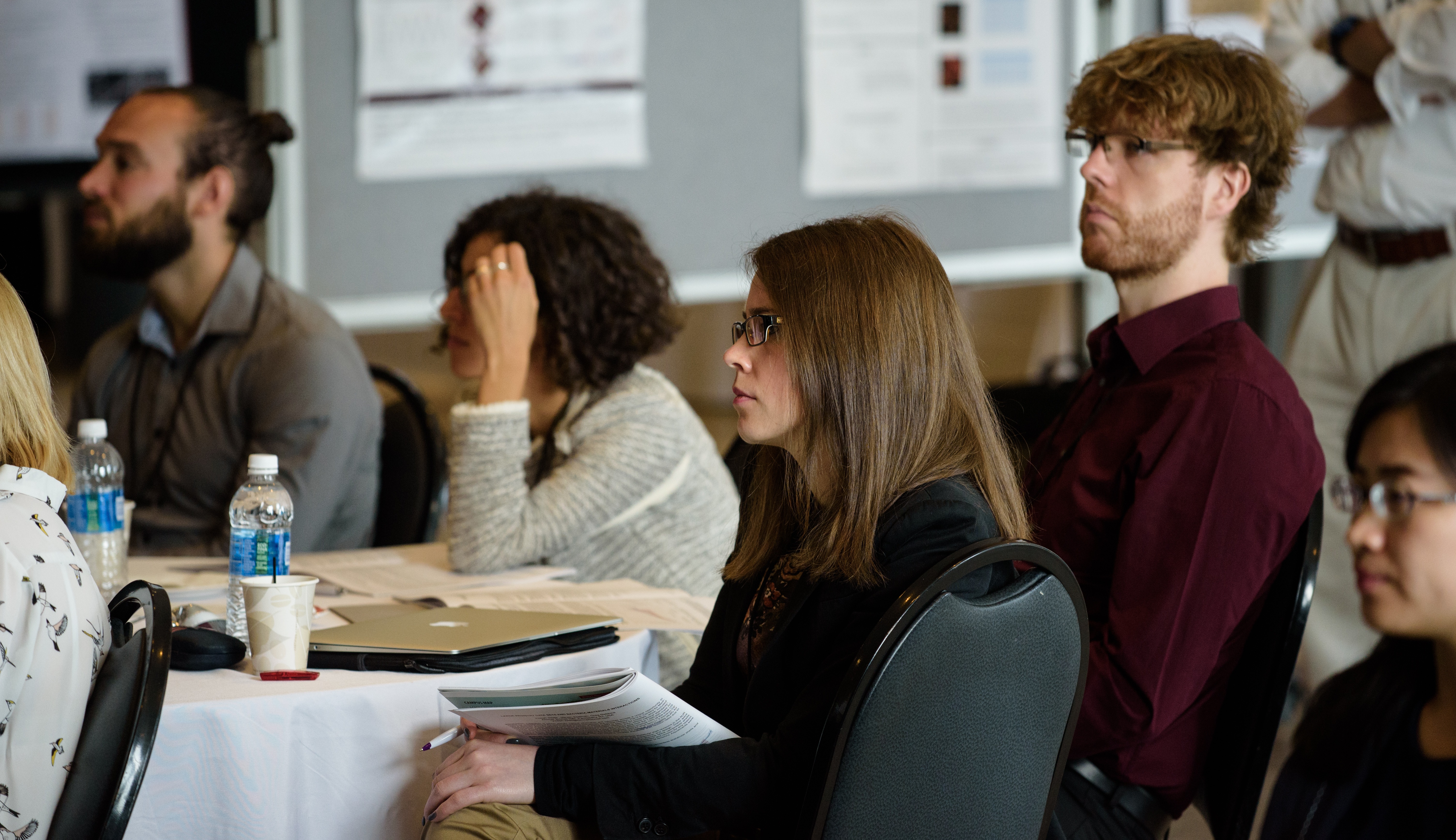 A group of people sitting at a round table in a conference room, attentively listening to a presentation.