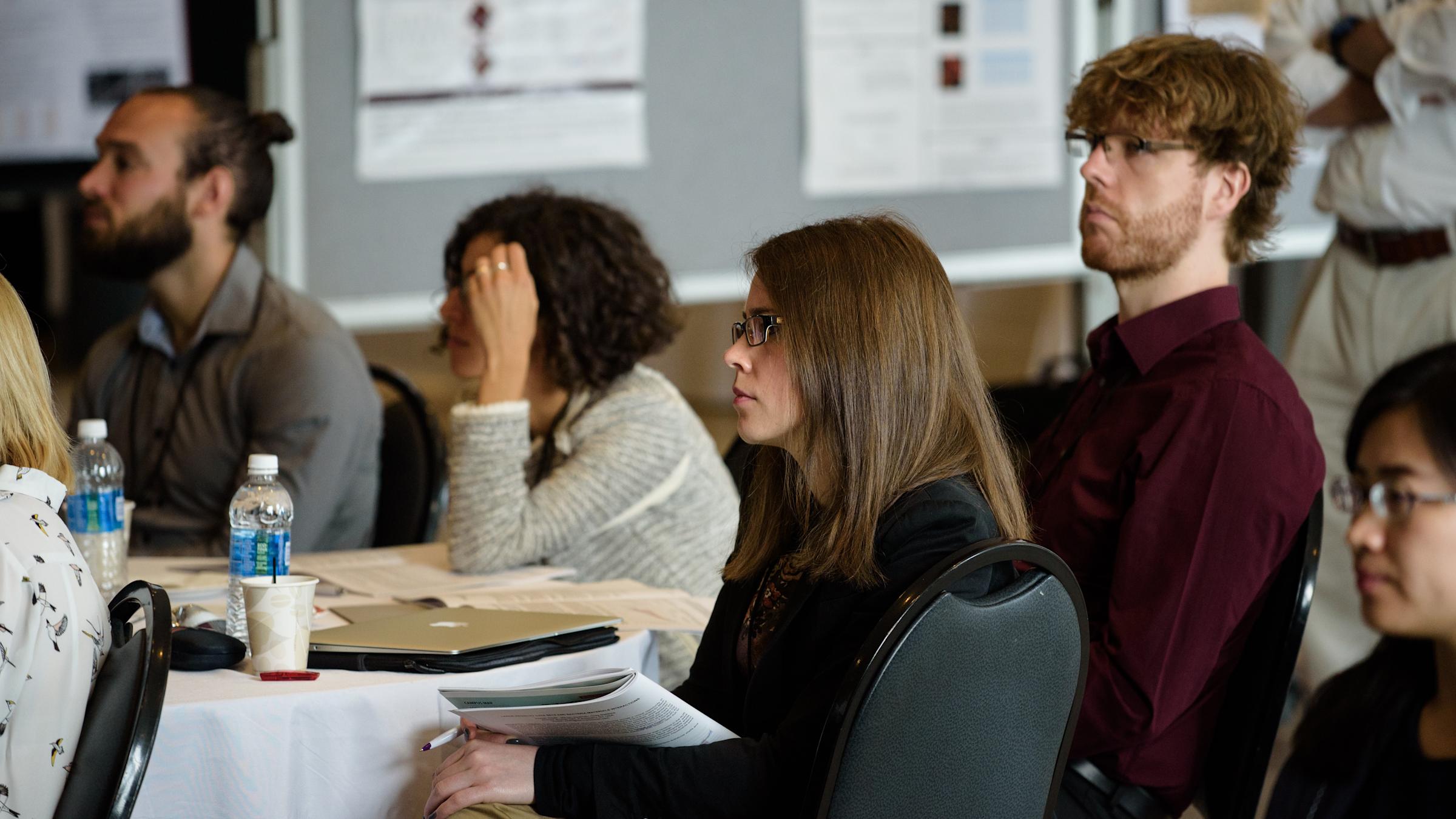 A group of people sitting at a round table in a conference room, attentively listening to a presentation.