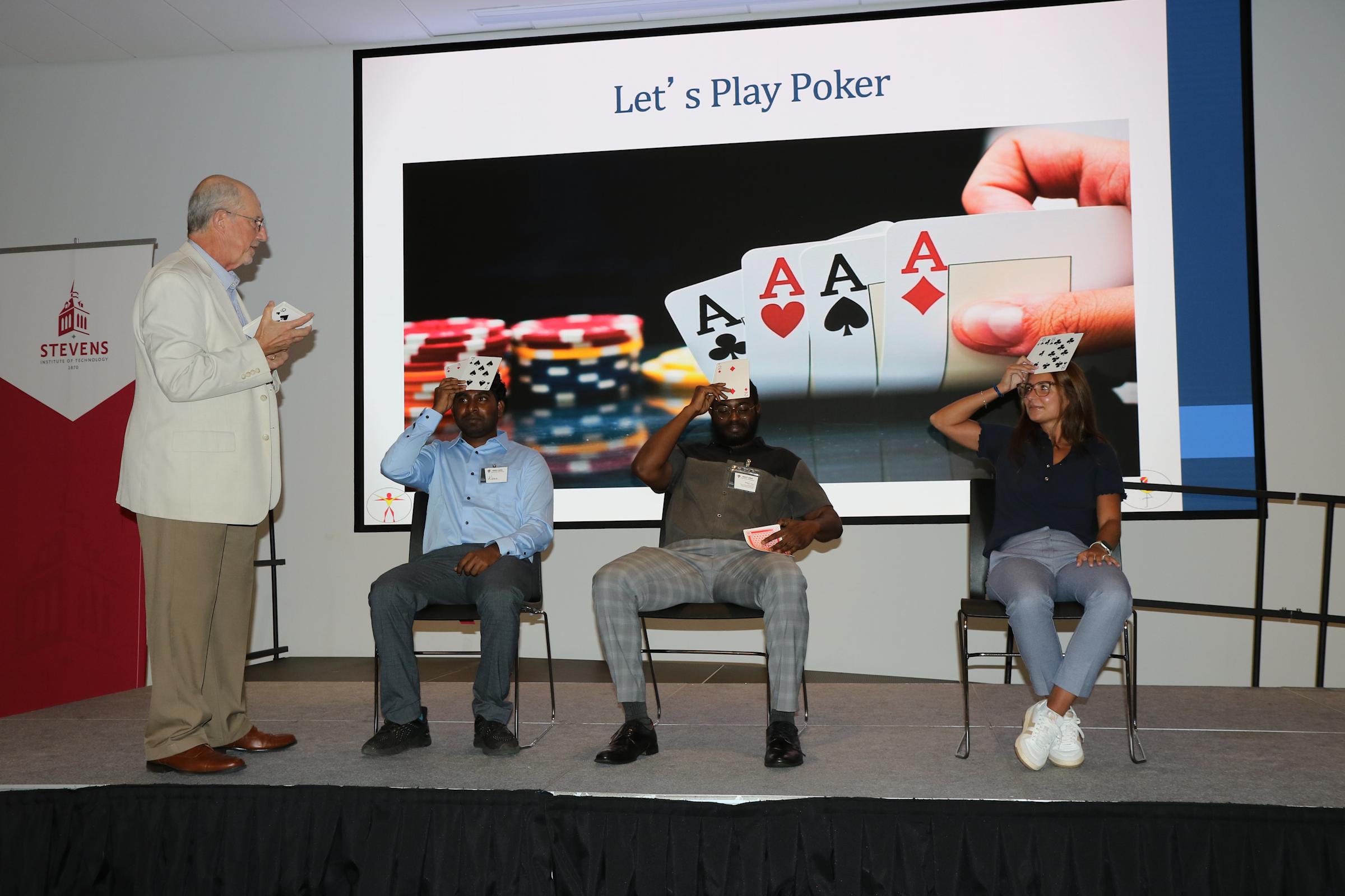 Randall Ribaudo playing a alternate game of poker on stage with three students holding cards atop their heads.