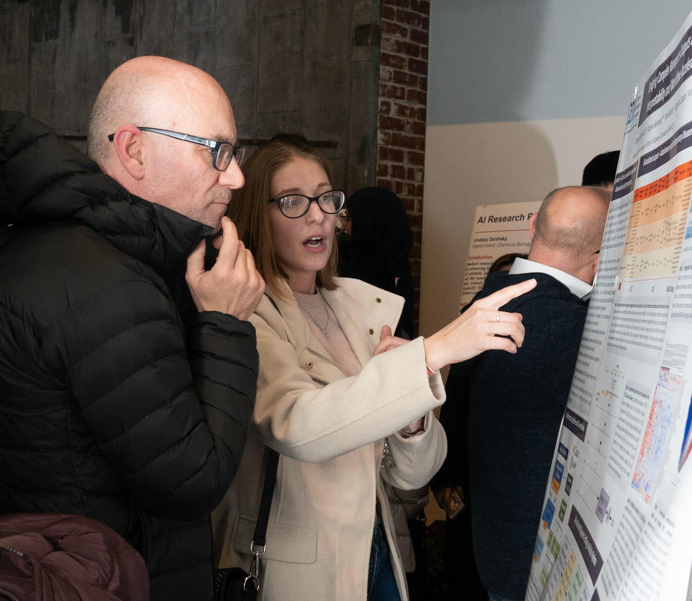 Professor Marcin Iwanicki examines a presentation board with a seminar attendee pointing at it.