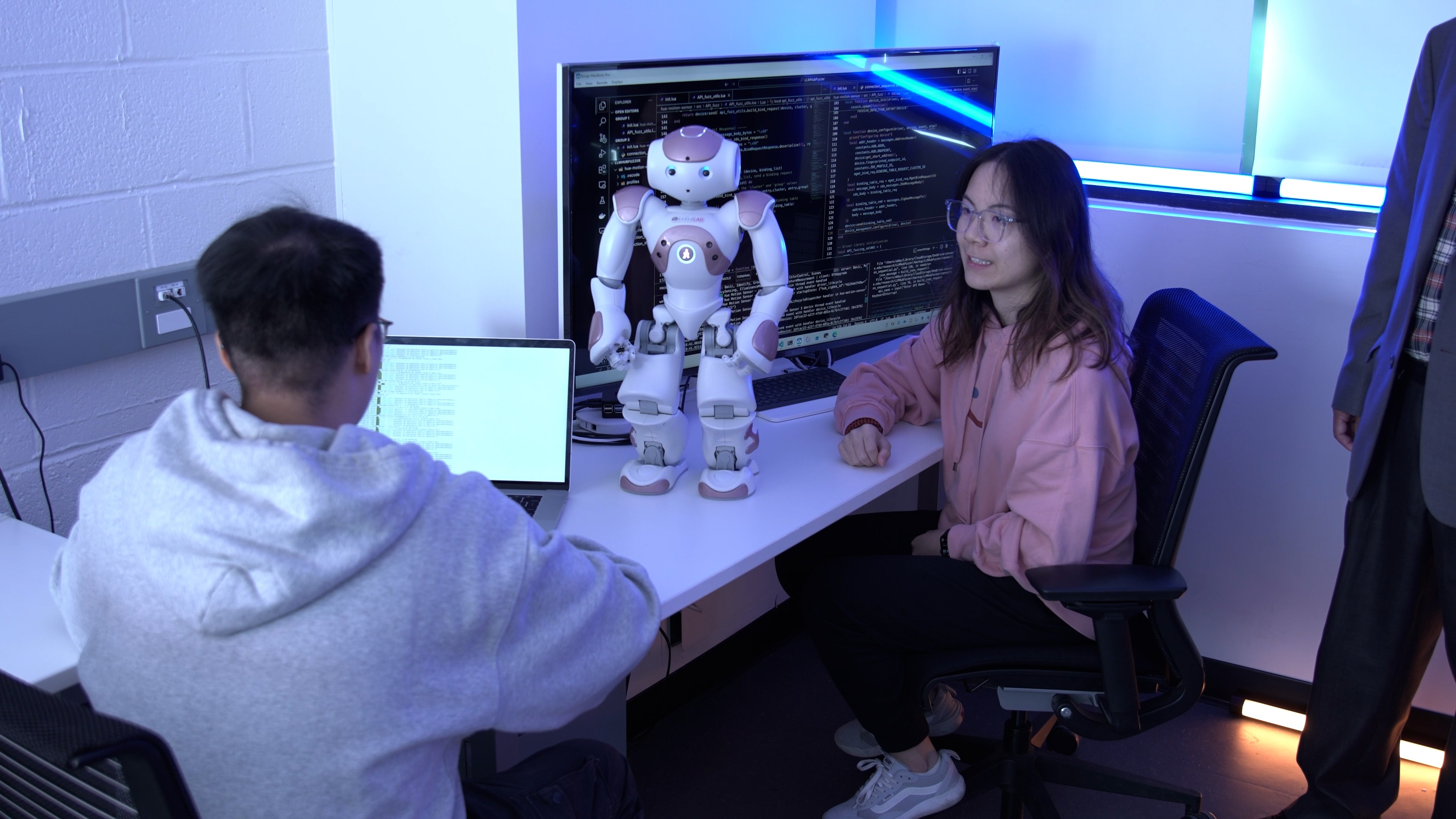 Two students sit at a desk with a standing robot.