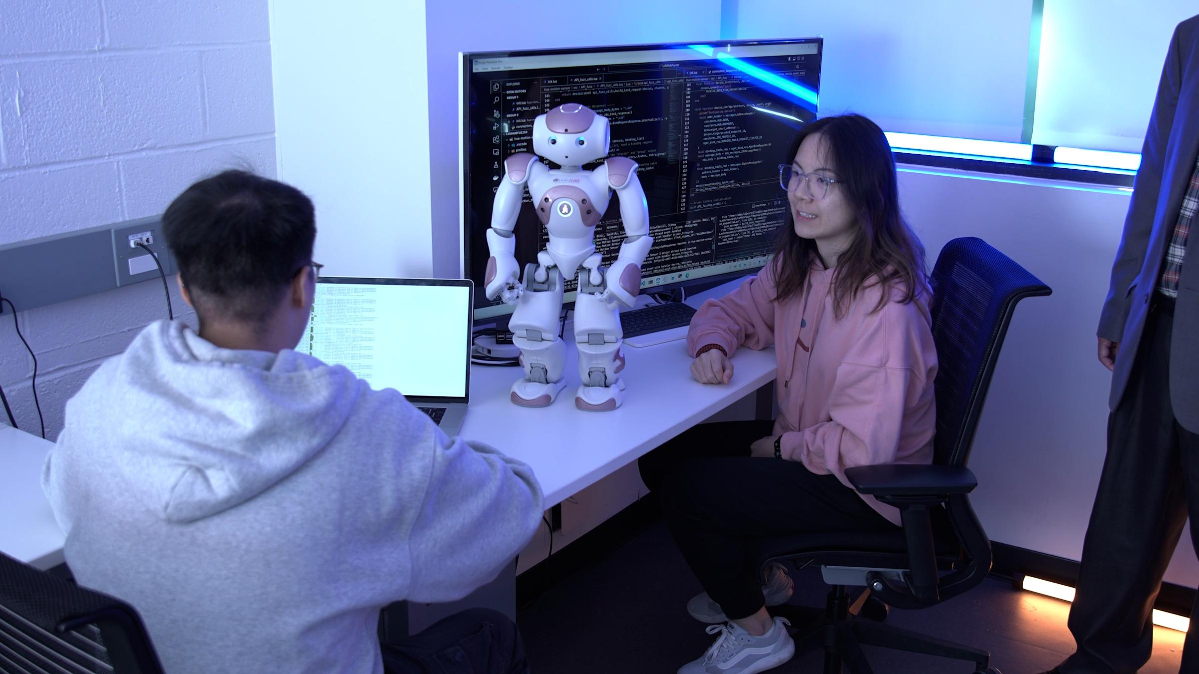 Two students sit at a desk with a standing robot.