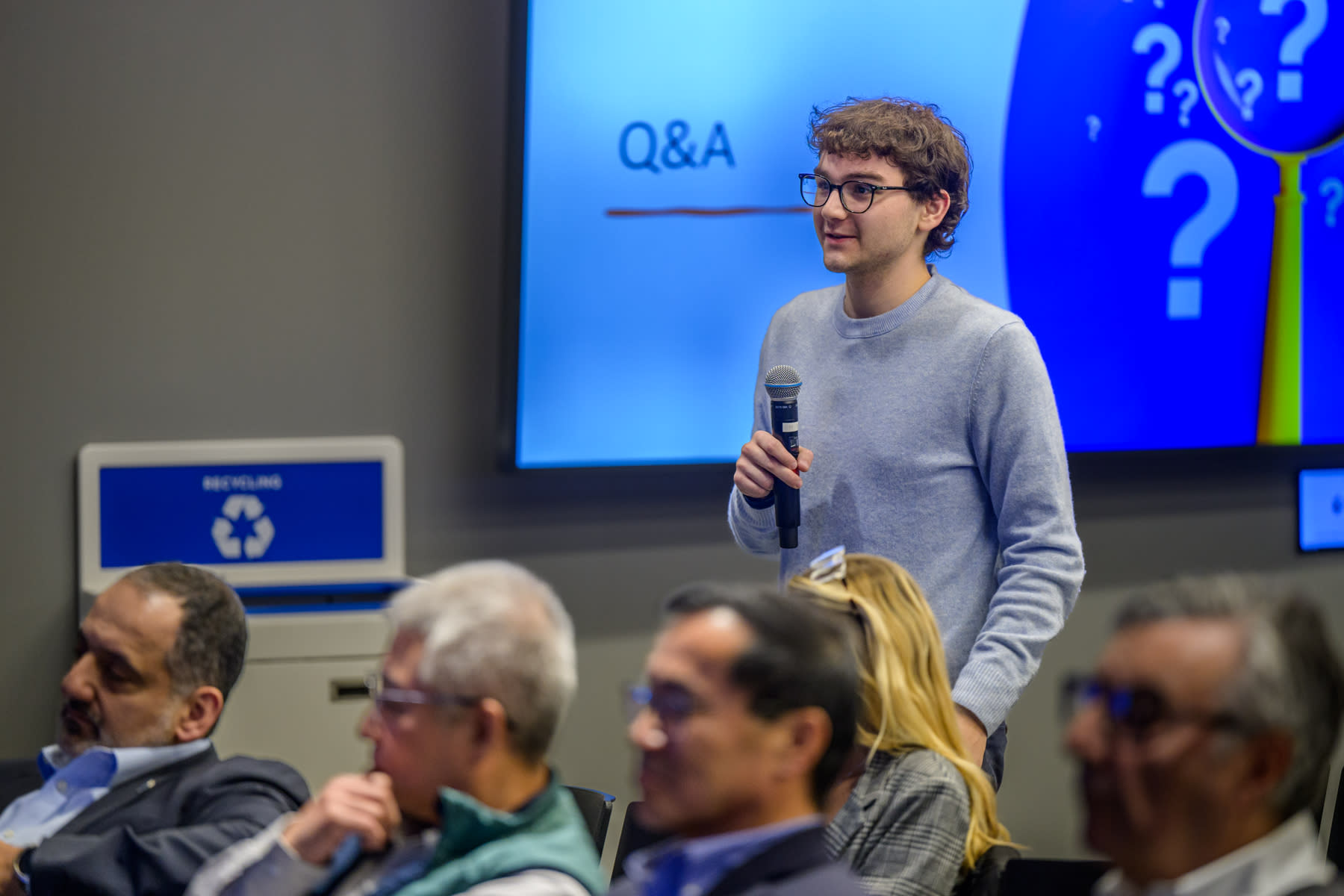 A Stevens student holding a microphone with a screen that reads Q and A behind him.