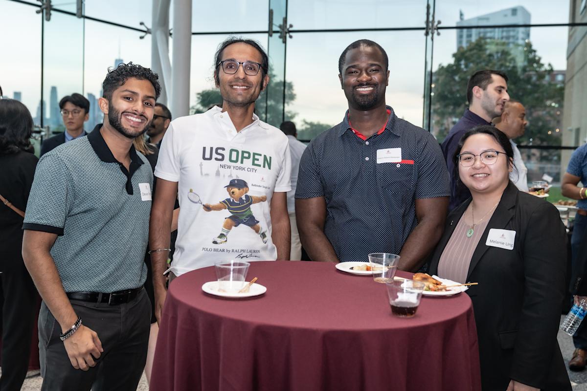 Four students pose for a photo standing around a cocktail table in the lobby of the Babbio Center.