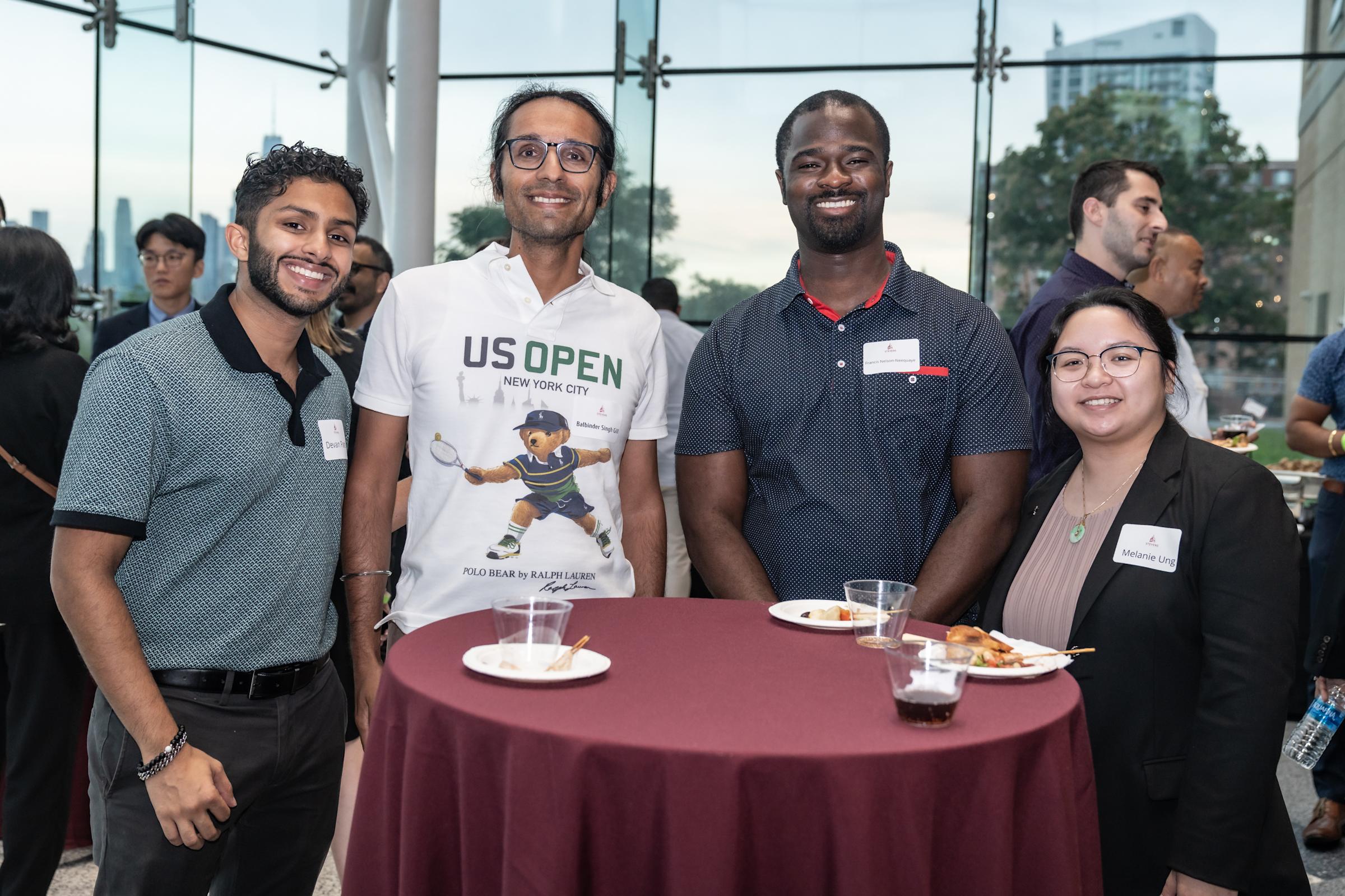 Four students pose for a photo standing around a cocktail table in the lobby of the Babbio Center.