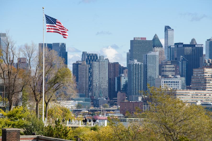 American flag flys on Stevens campus at Castle Point with New York city in background.