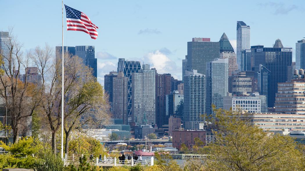 American flag flys on Stevens campus at Castle Point with New York city in background.