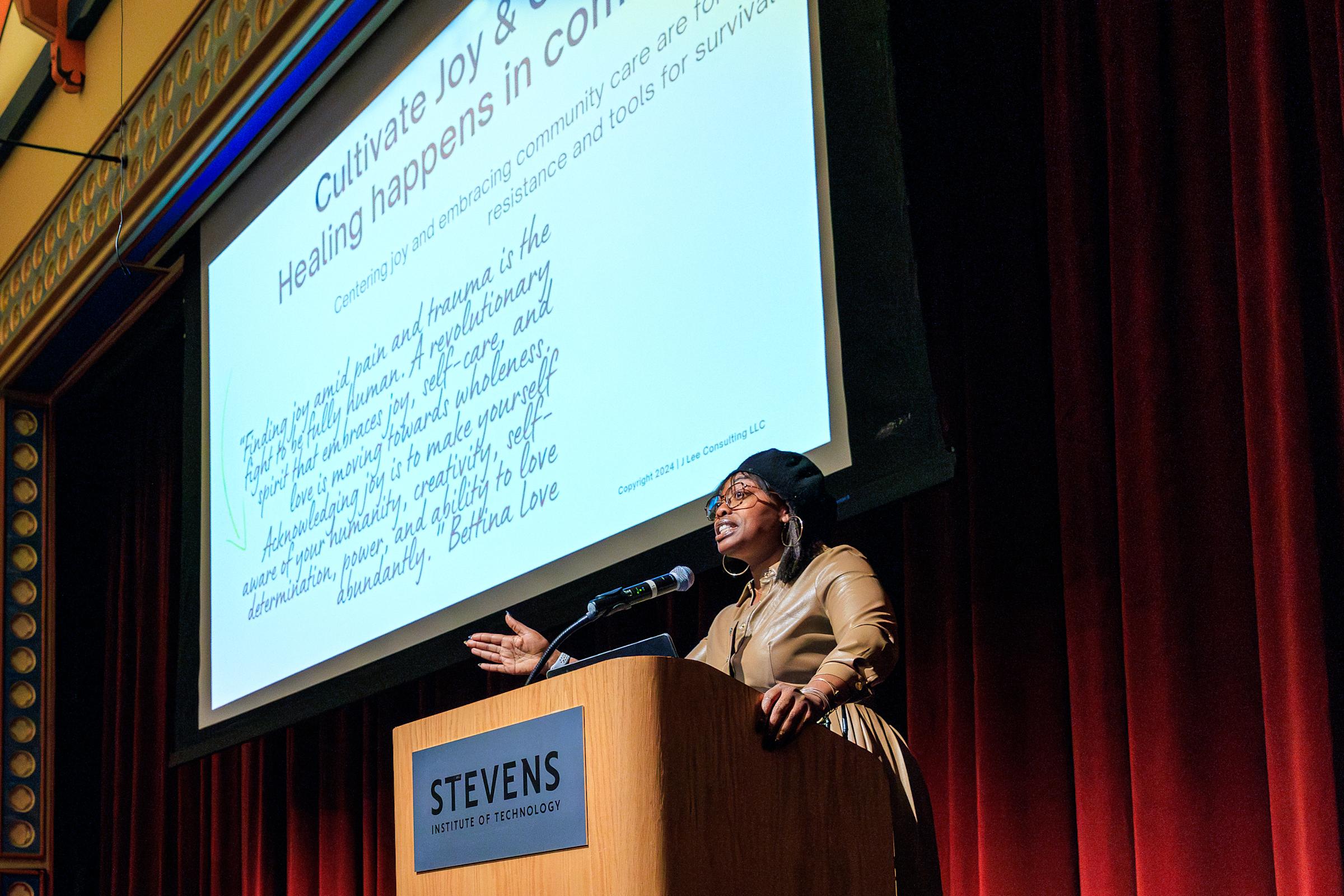 A woman delivers a talk at a podium with a large projection screen behind her