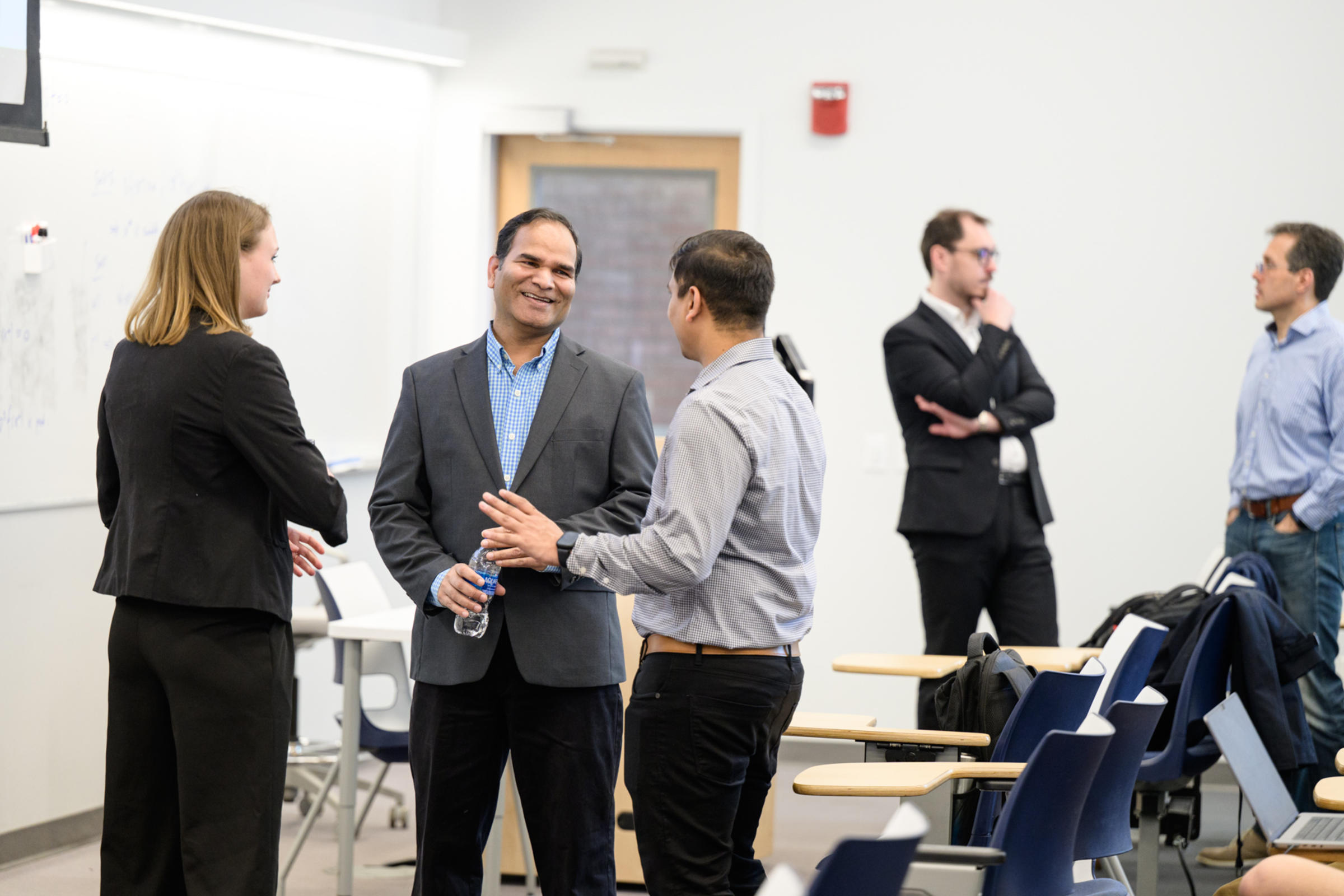A woman on the left, and four men to the right of her, all talking together and having a conversation
