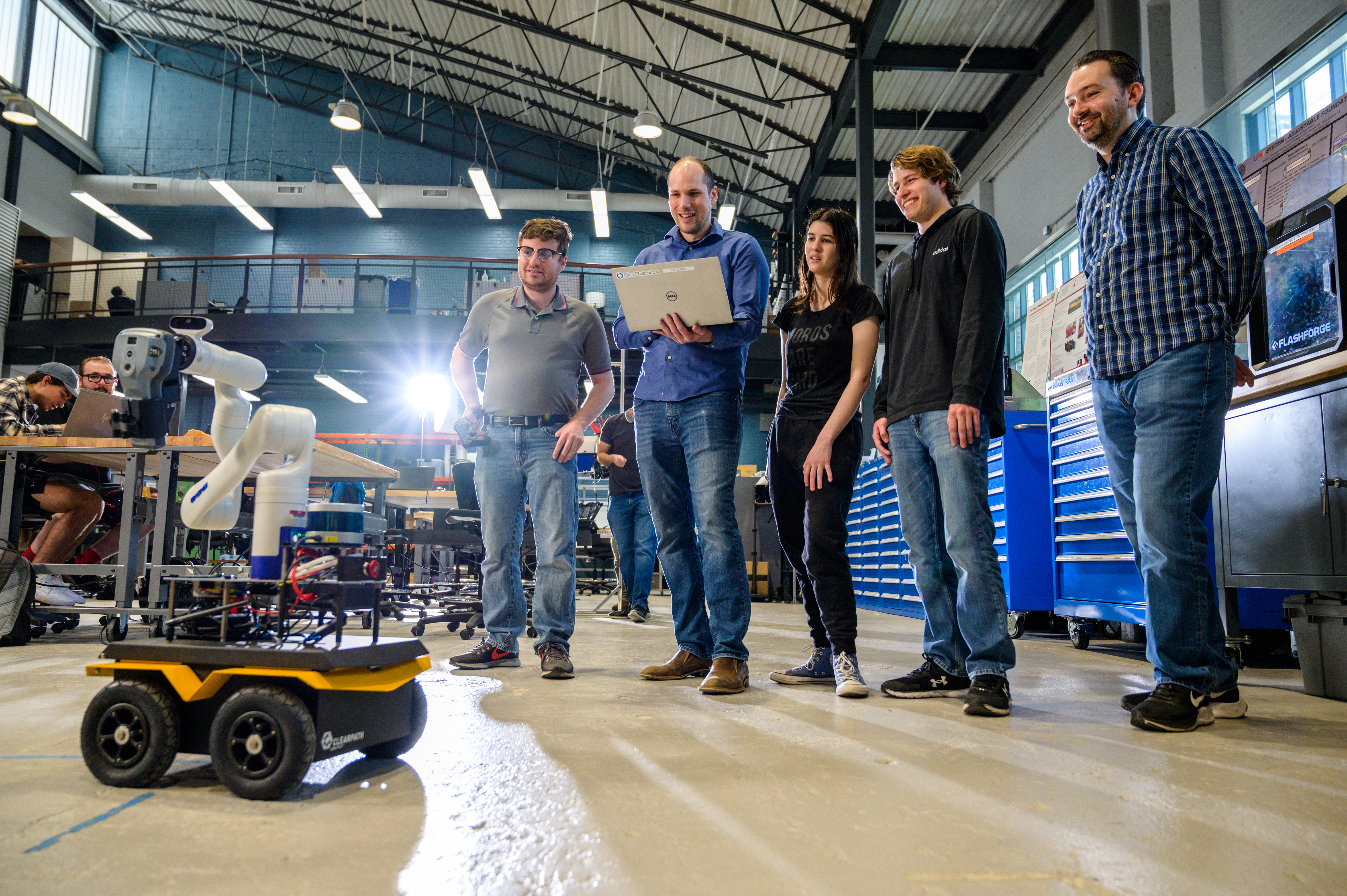 Three male students and a female student smiling with professor Brendan Englot in a lab testing a robot