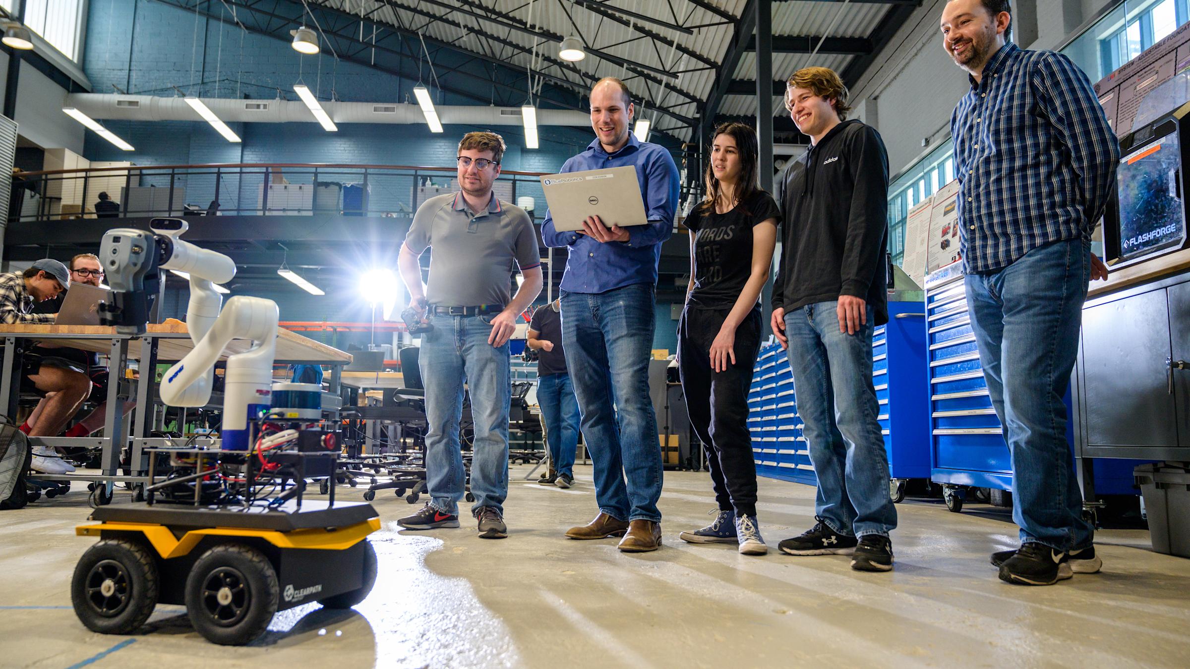Three male students and a female student smiling with professor Brendan Englot in a lab testing a robot