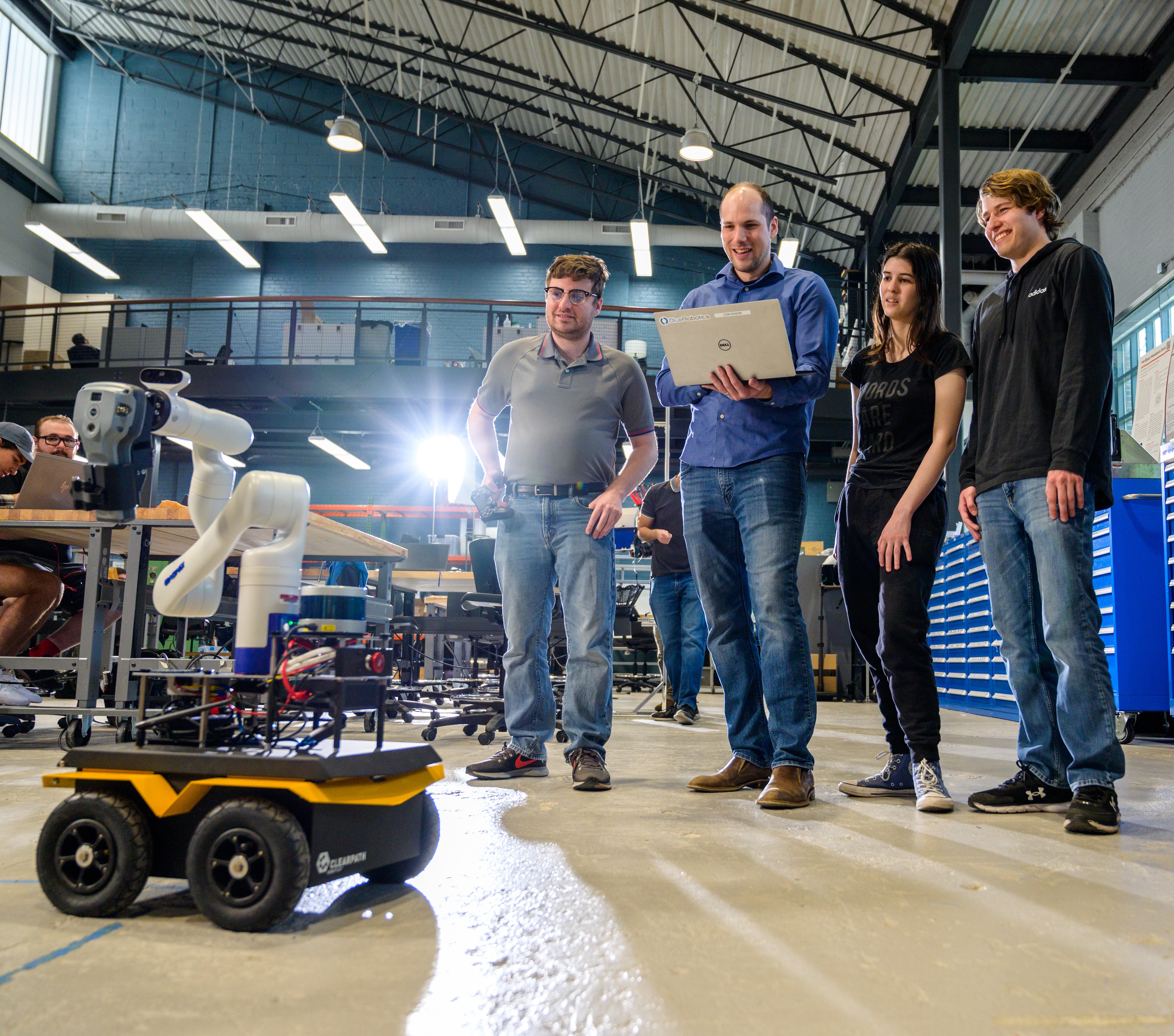 Three male students and a female student smiling with professor Brendan Englot in a lab testing a robot
