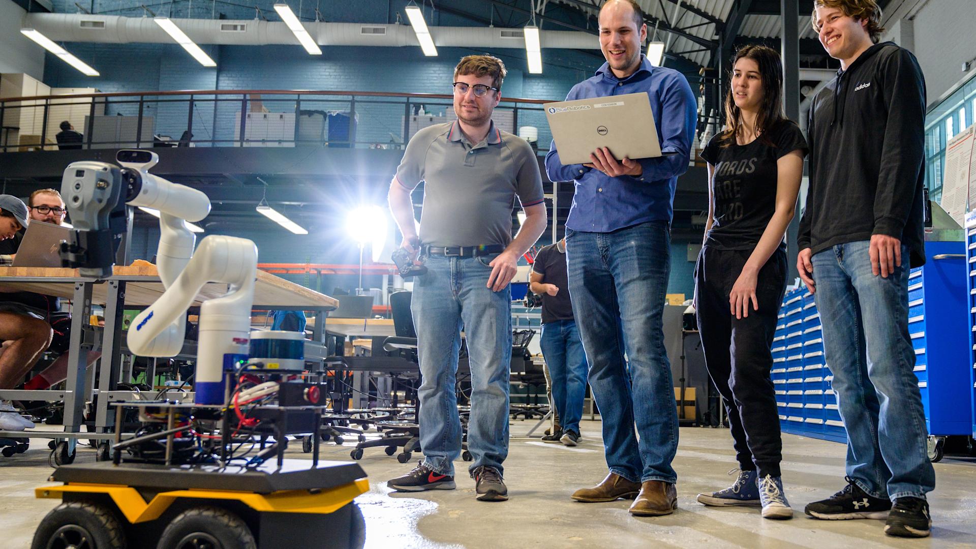 Three male students and a female student smiling with professor Brendan Englot in a lab testing a robot