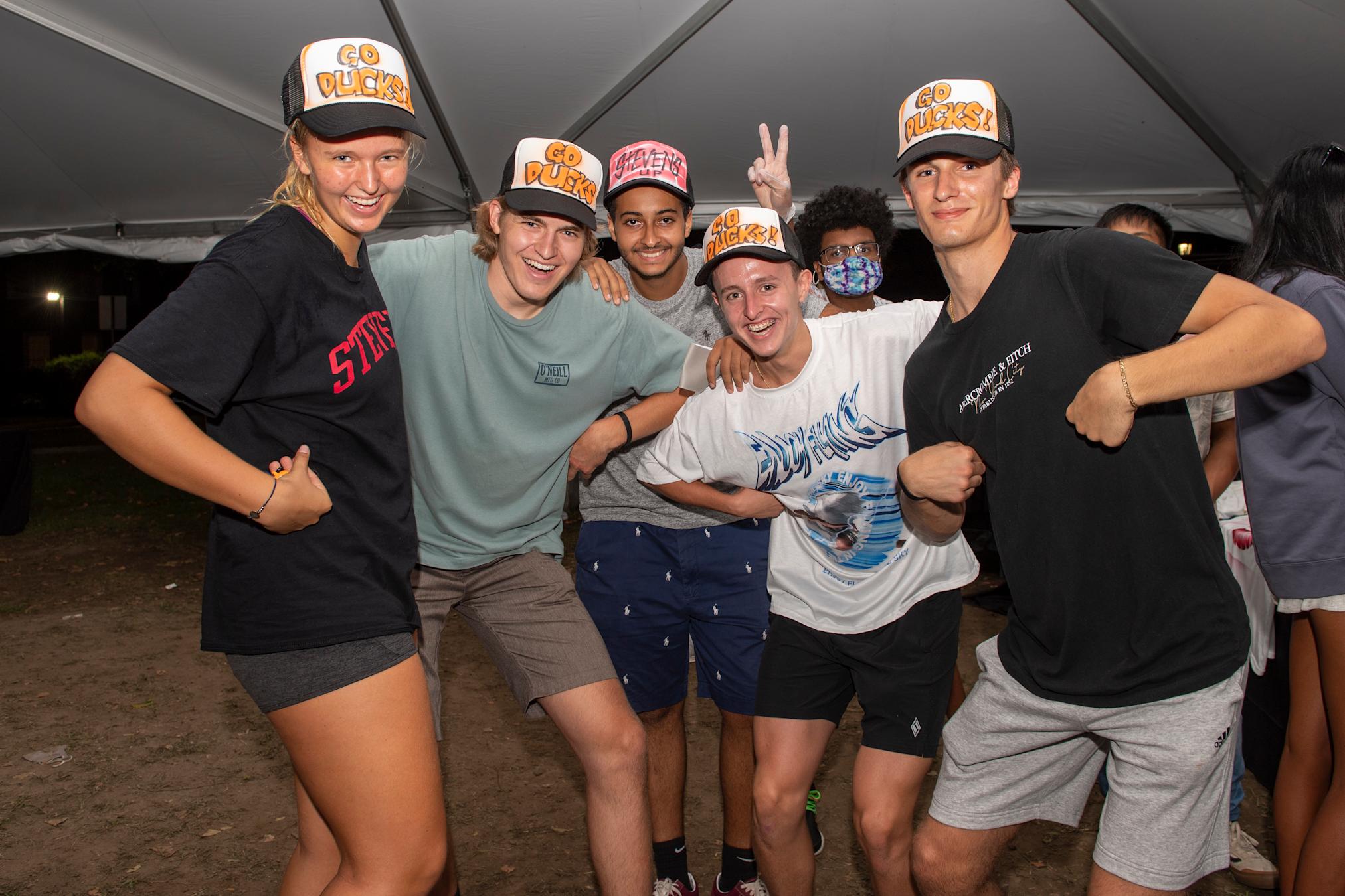 Group of students laughing while pretending to be ducks wearing "Go Ducks" trucker caps