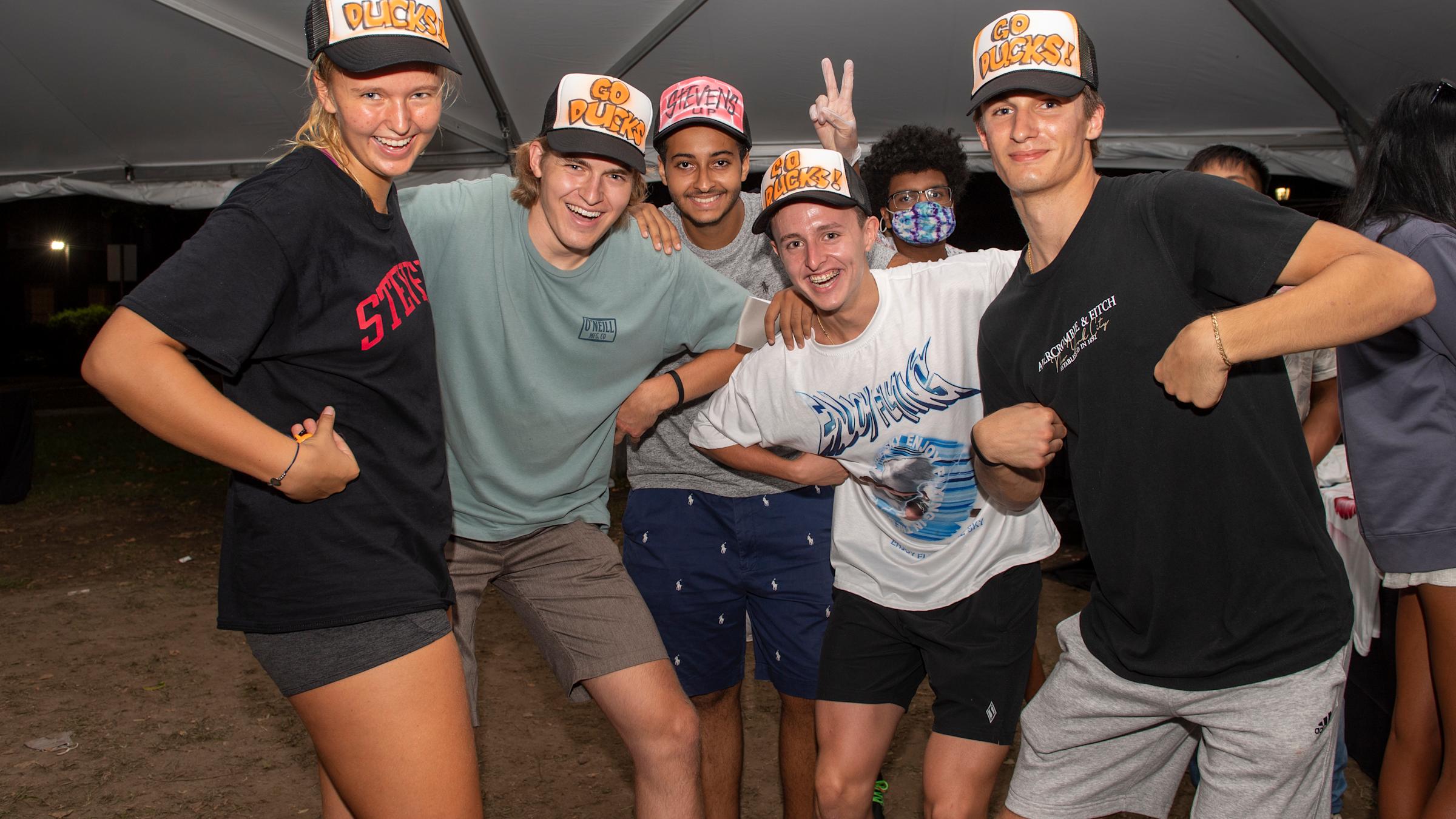 Group of students laughing while pretending to be ducks wearing "Go Ducks" trucker caps
