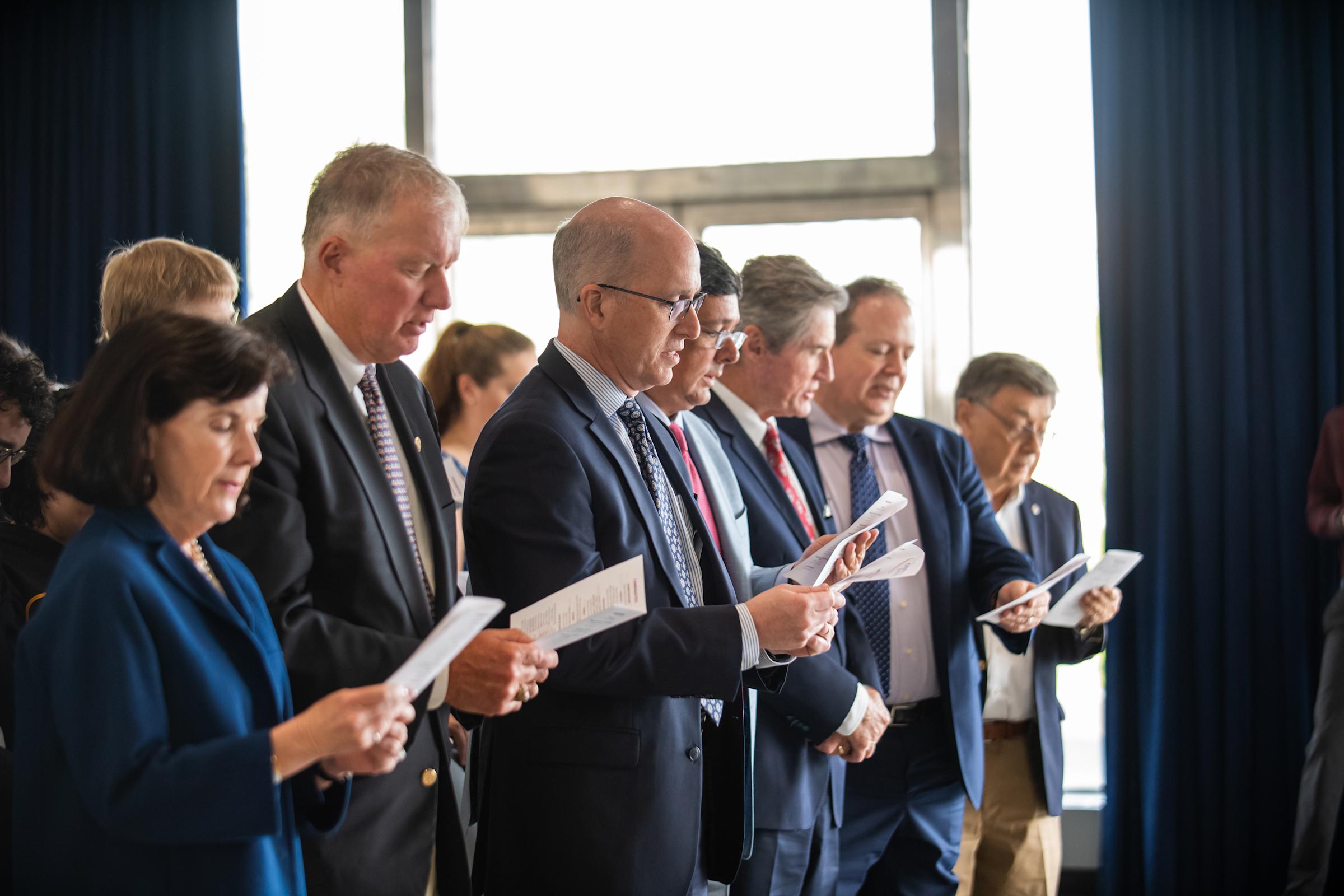 Photo of standing Trustees and alumni reading aloud/reciting the oath