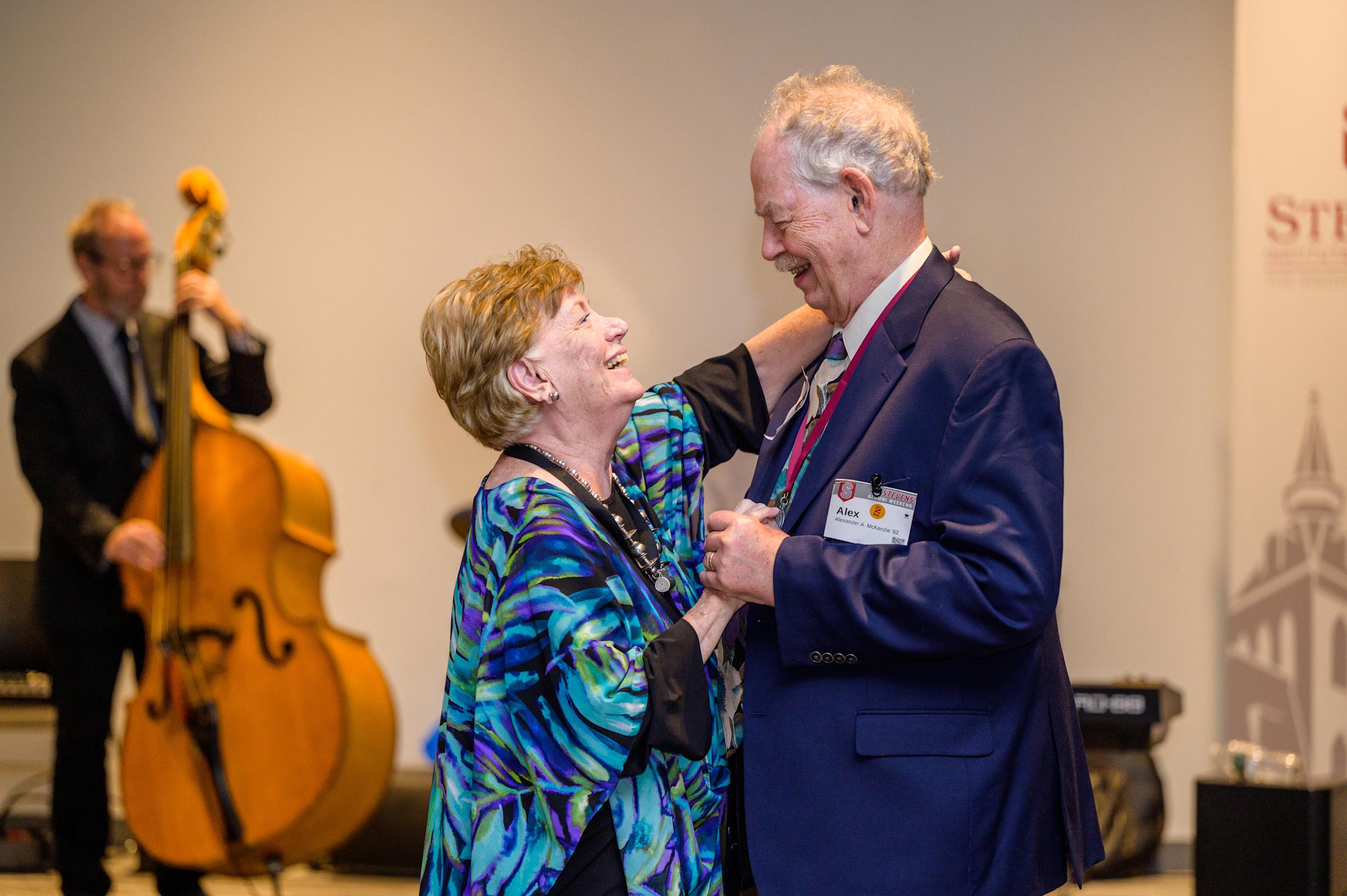 A couple smiles at each other as they dance with a stand up bassist playing music int he background.