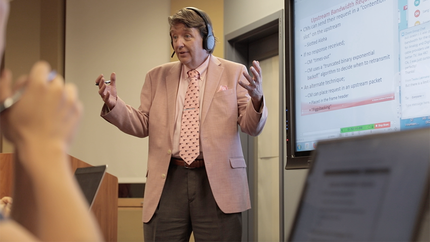 Kevin Ryan teaching in front of a screen in a hybrid classroom.