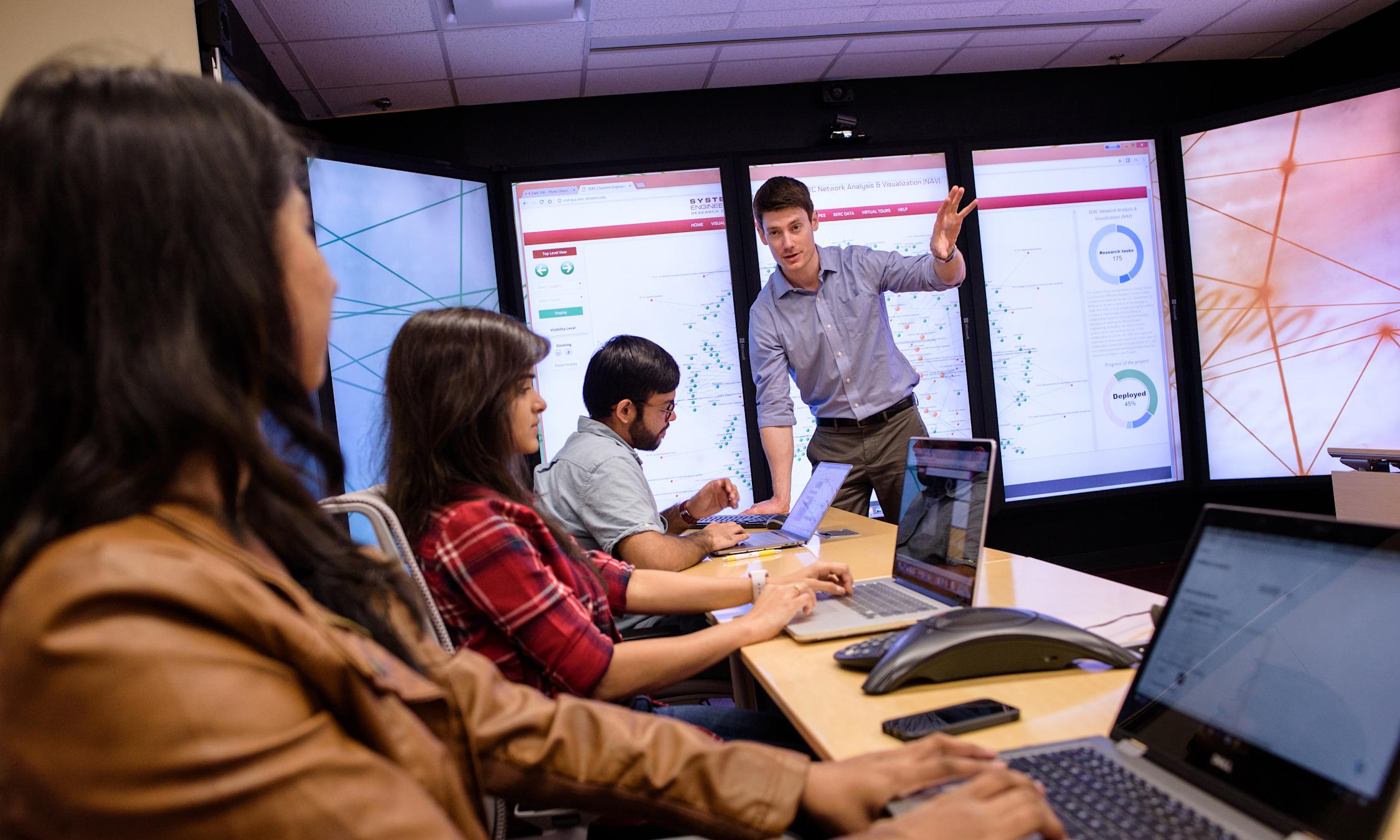 Professor gestures to explain concept in class in front of immersive video wall