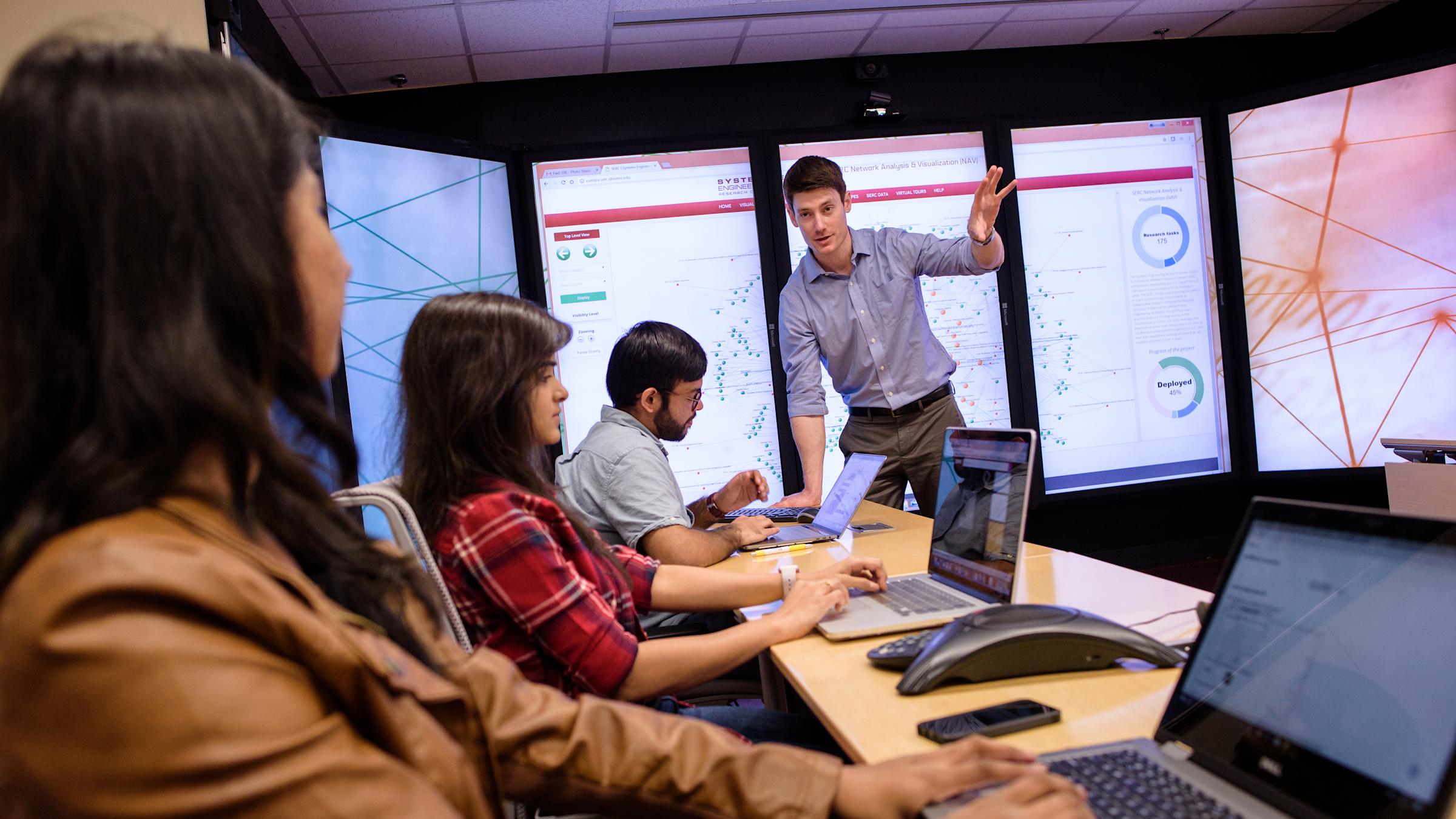 Professor gestures to explain concept in class in front of immersive video wall