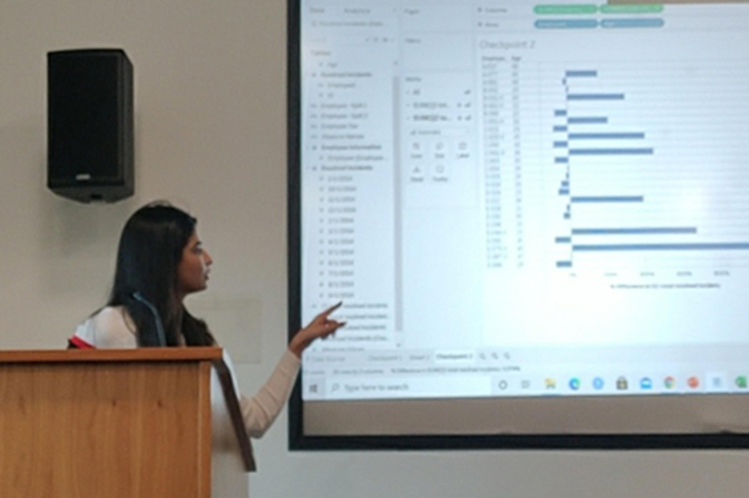 Aayushi Ghandi teaching in front of a class. A projection covers the back wall.