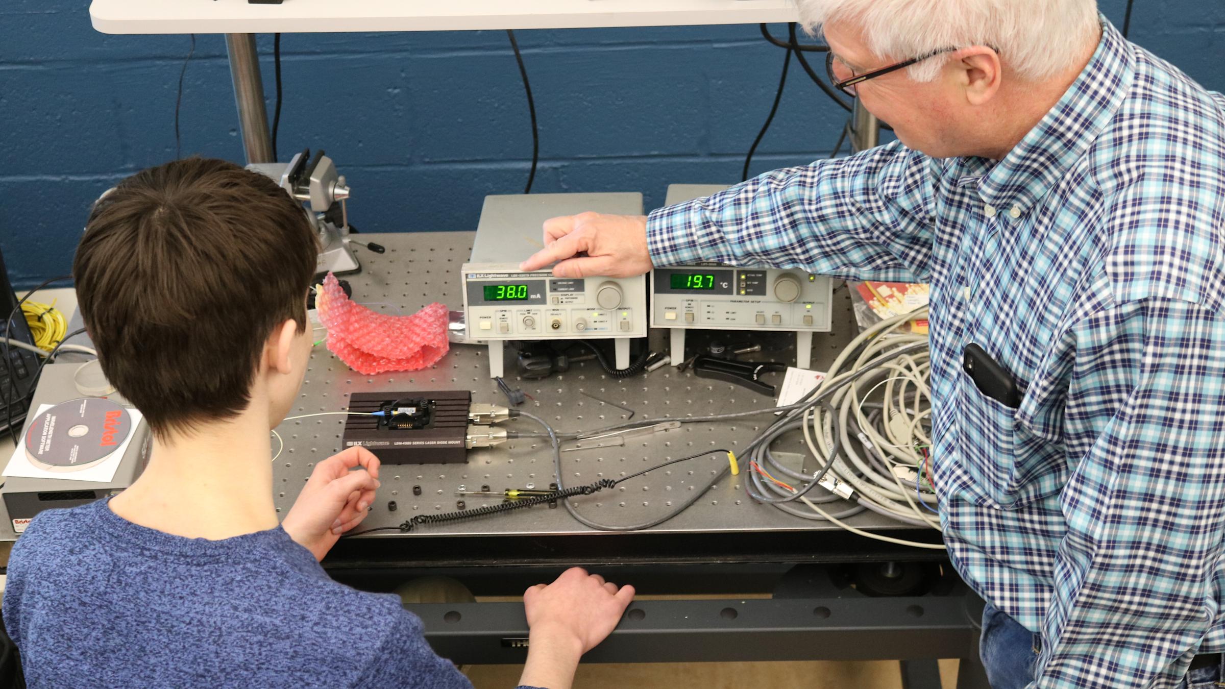 A student and faculty member working with equipment inside of a Physics lab.