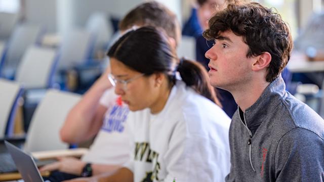 Two students in class taking notes during a lecture.