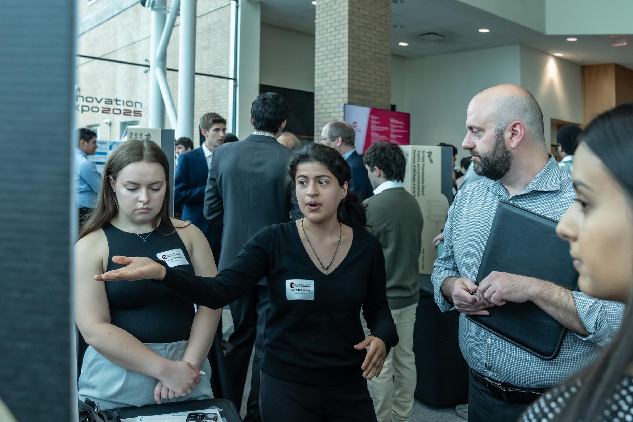 A student in a black dress presents her project to a visitor at her display.