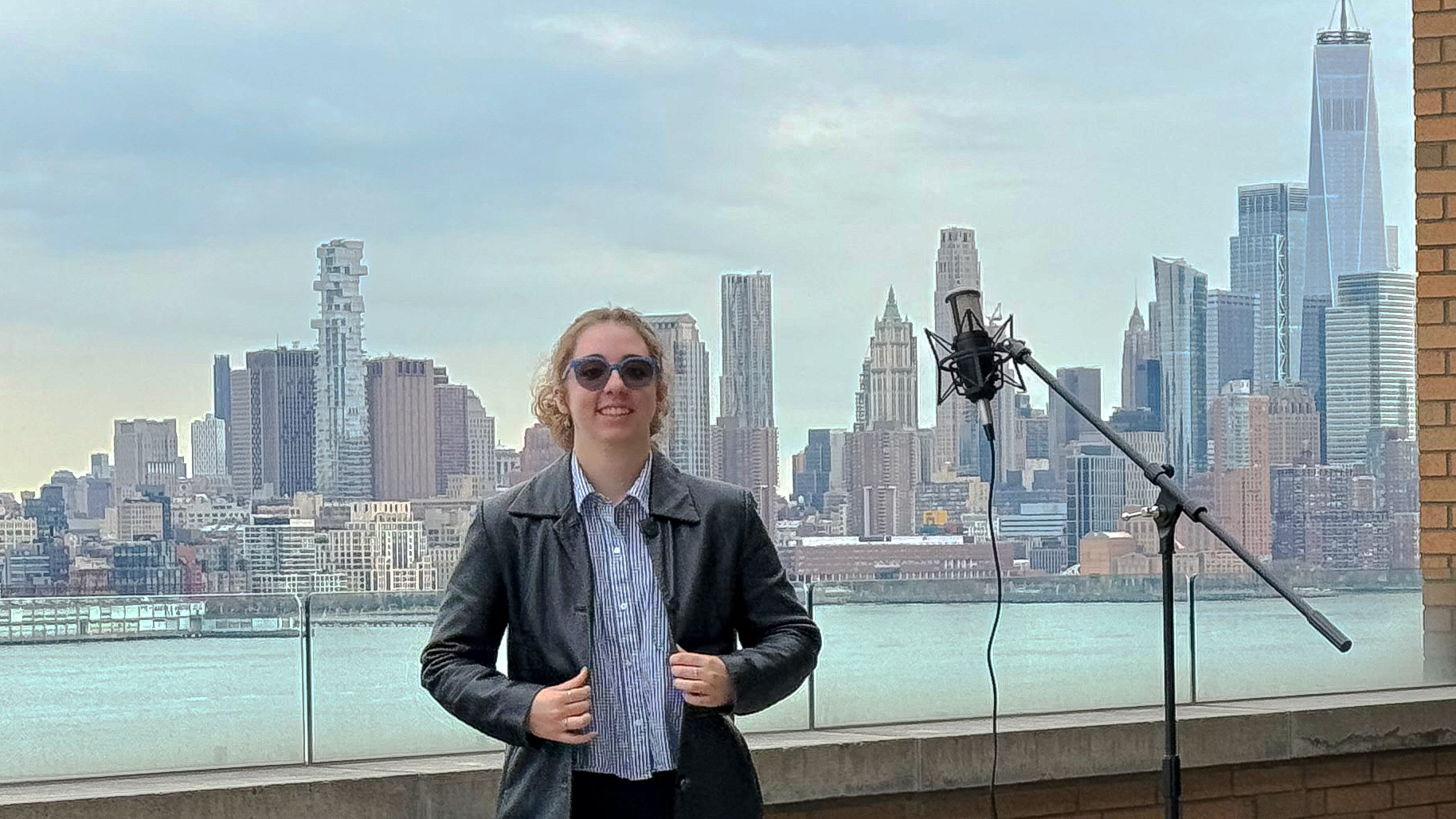 A young woman with sunglasses and a leather jacket poses on Stevens' campus with the New York City skyline in the background.