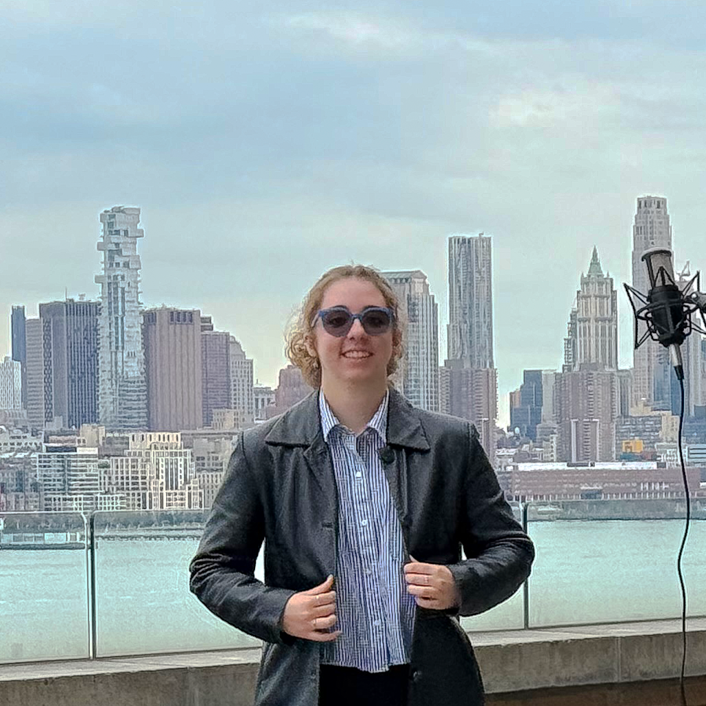A young woman with sunglasses and a leather jacket poses on Stevens' campus with the New York City skyline in the background.
