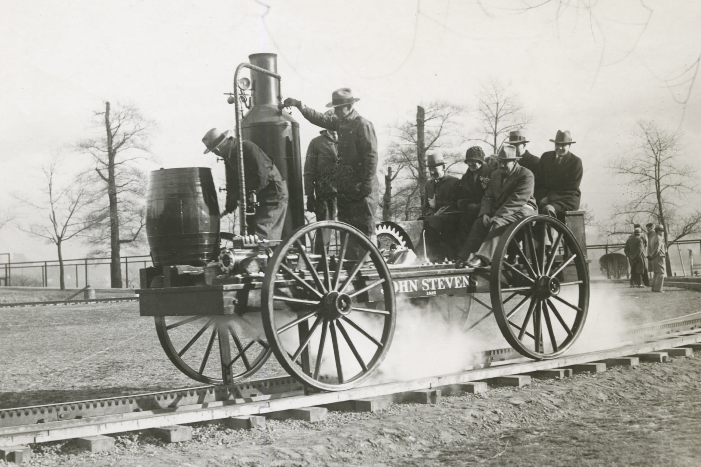 Black and white photo of small steam locamotive on circular track with about 8 people aboard.