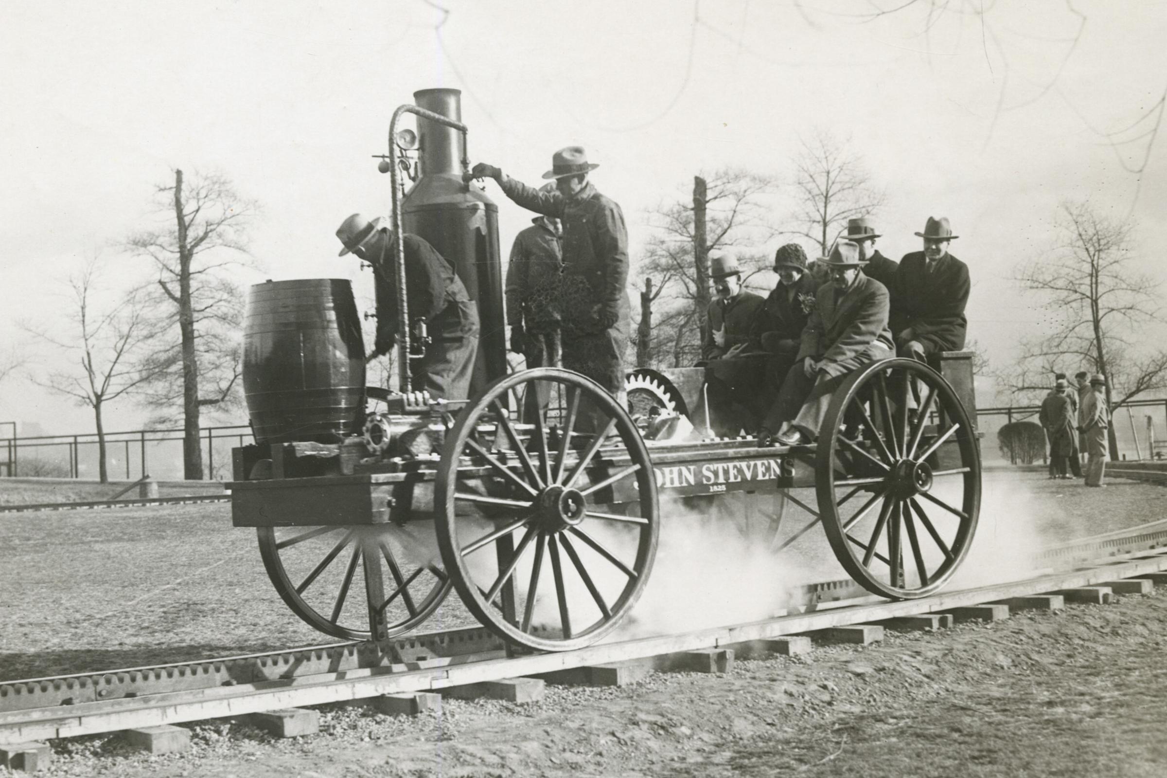 Black and white photo of small steam locamotive on circular track with about 8 people aboard.