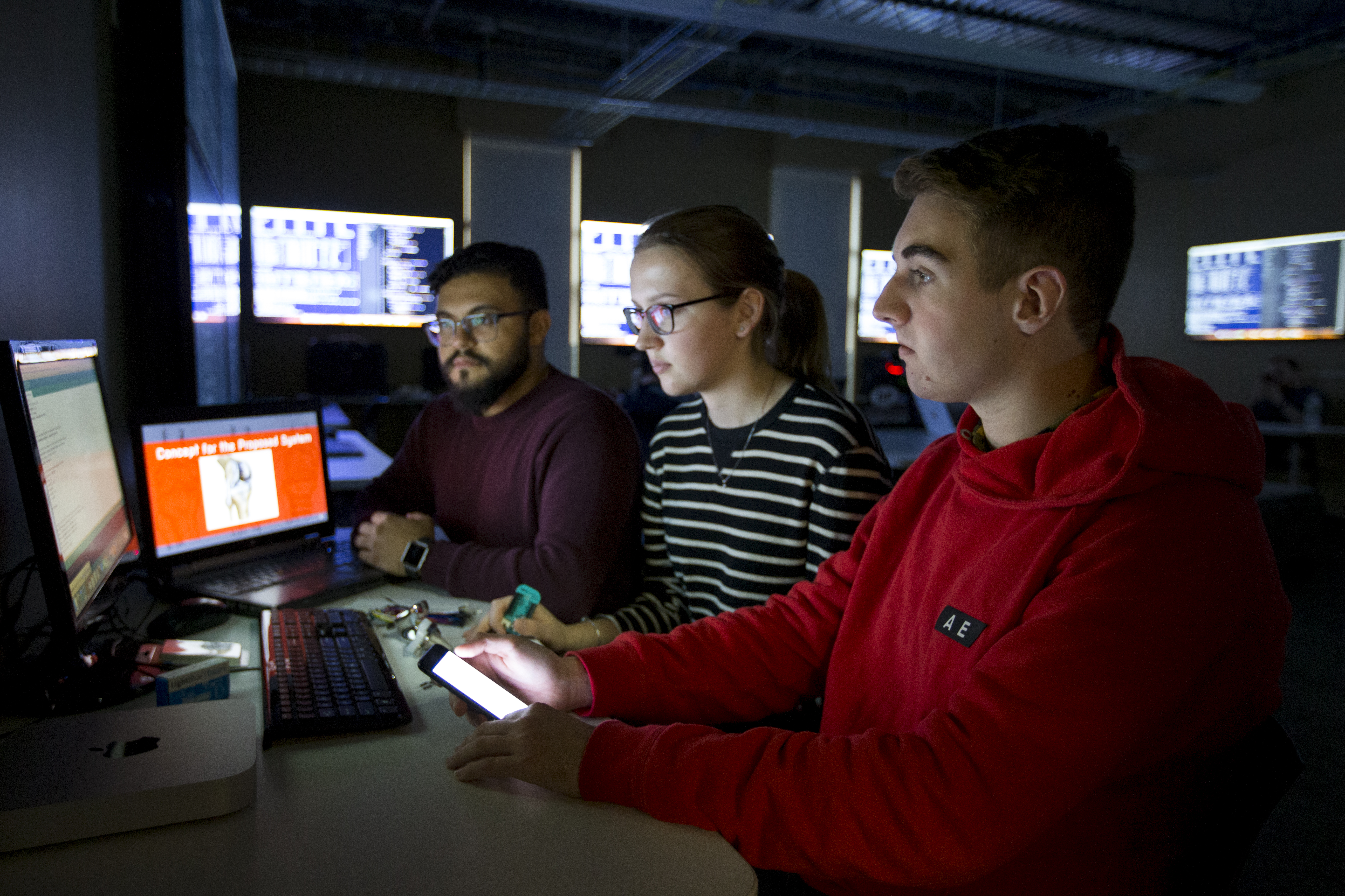 Three students looking at a laptop in dark room